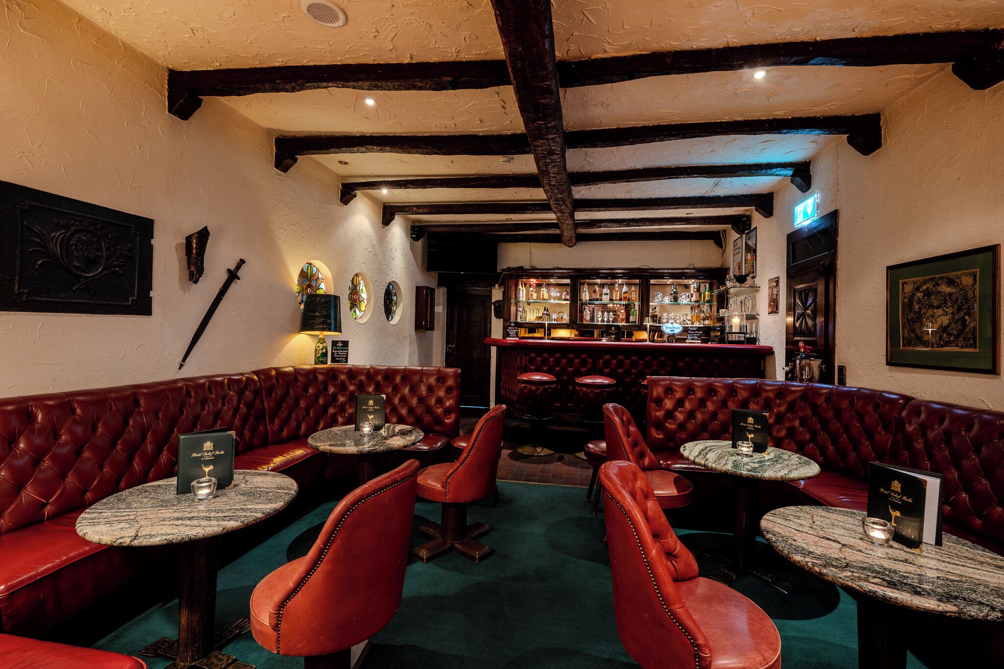A cozy bar with leather booths and round tables, featuring a rustic ceiling and a well-stocked bar area.