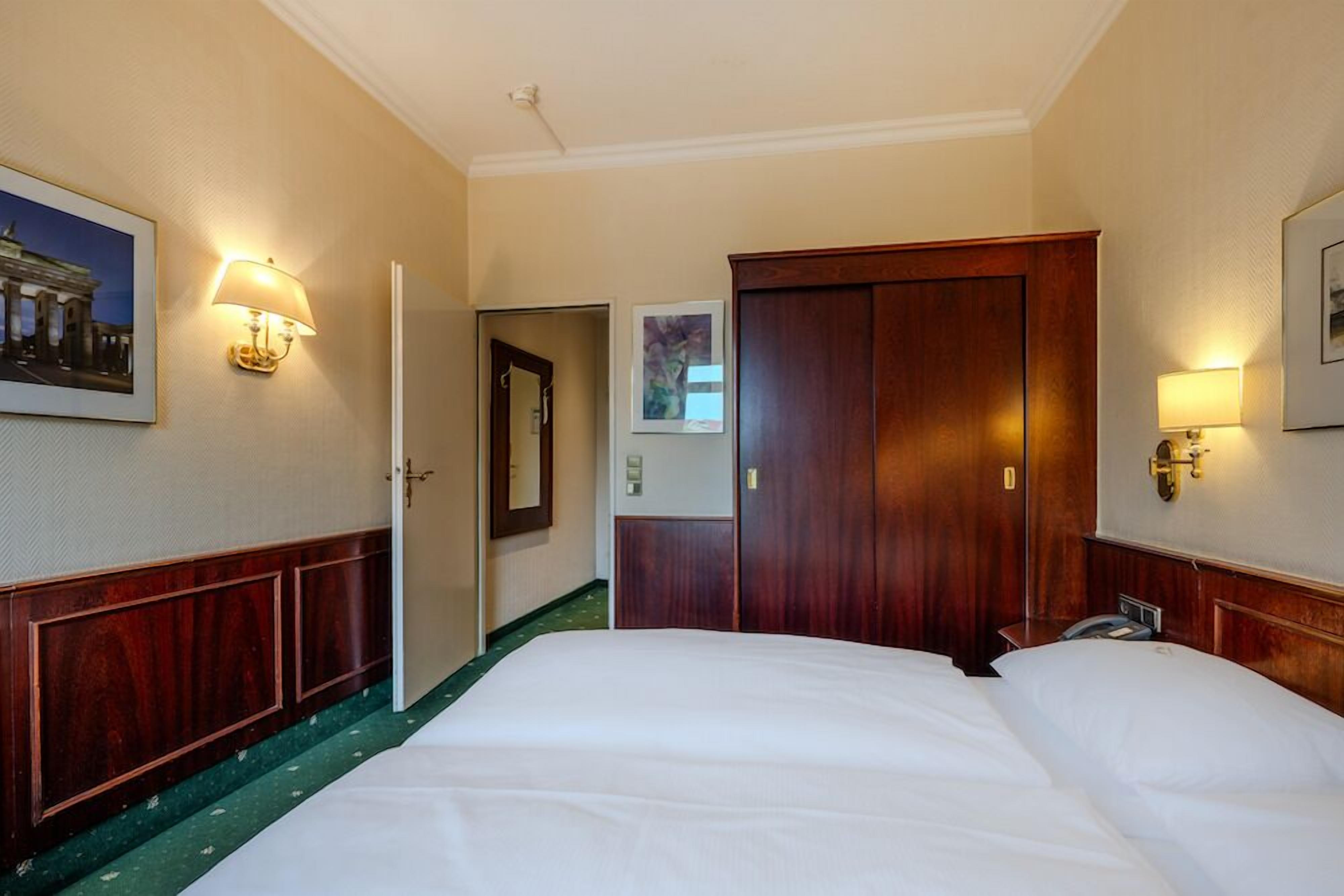 A hotel room with a large bed, wooden wardrobe, and two wall-mounted lamps.