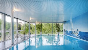 An indoor swimming pool with clear glass walls, potted plants, and a view of greenery outside. - Ringhotel Seehof Berlin (Berlin)