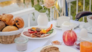 A breakfast table with croissants, a fruit plate, a pitcher, and a view of a lake. - Ringhotel Seehof Berlin (Berlin)