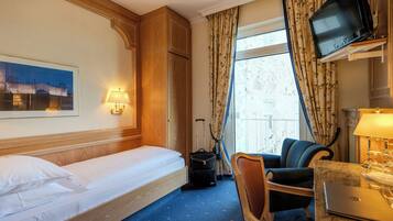 Habitación de hotel con una cama, un escritorio con una computadora portátil, una silla, un televisor y una ventana con cortinas.