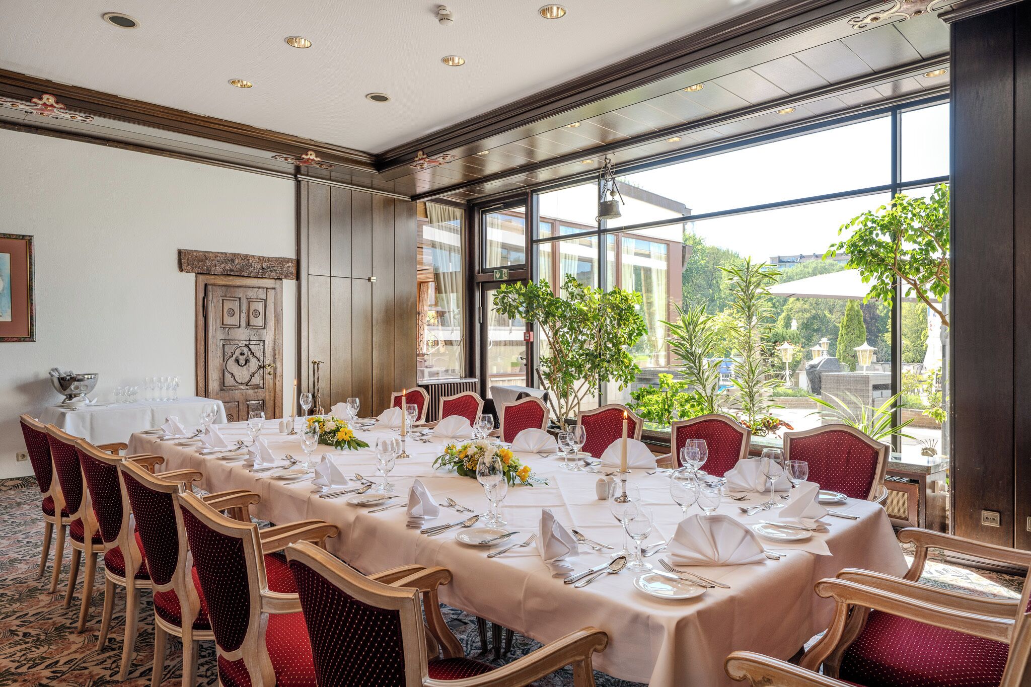 Une salle à manger avec une longue table dressée pour le repas, entourée de chaises à revêtement rouge.