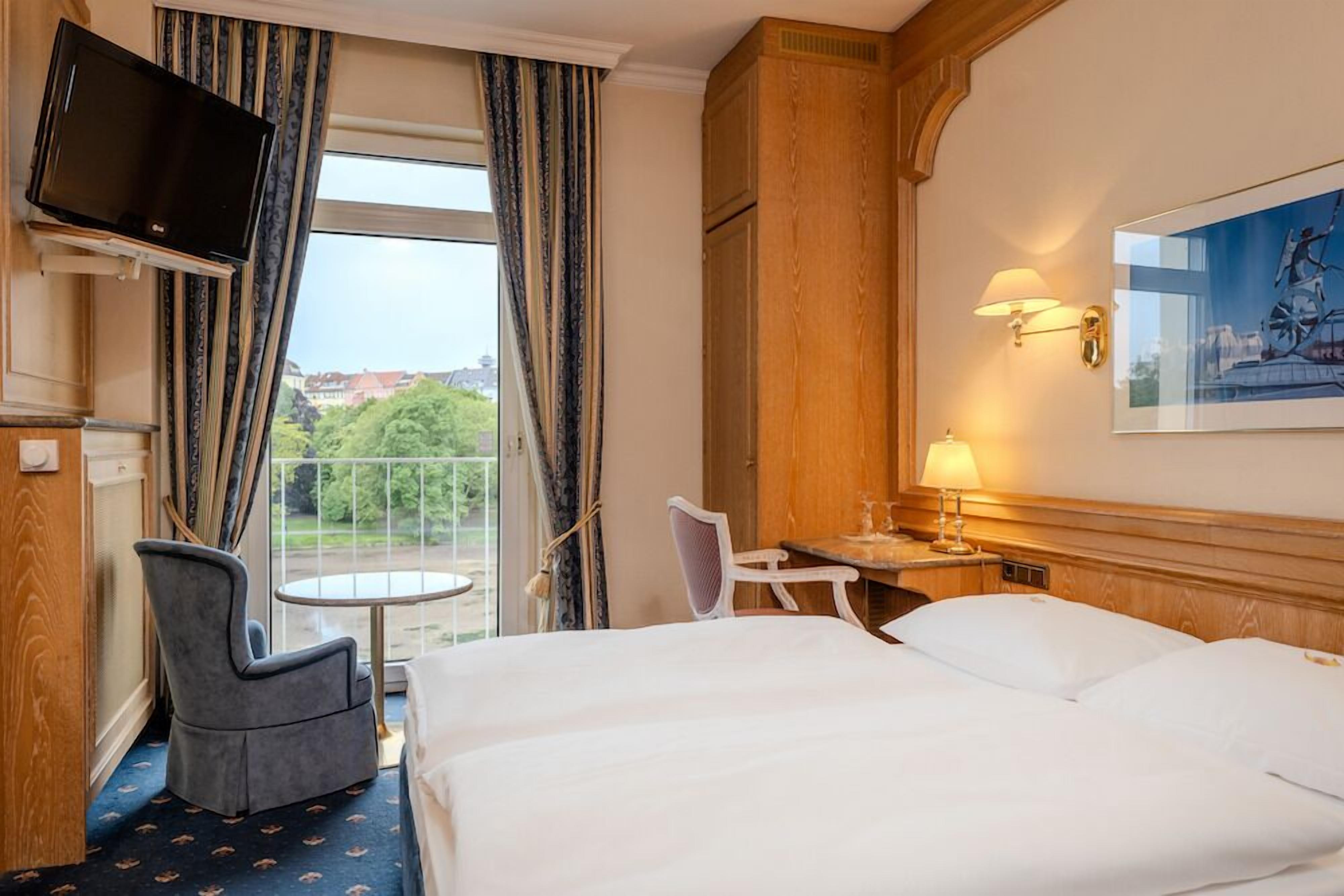 Une chambre d’hôtel équipée d’un lit, d’un bureau, d’une chaise, d’une télévision et d’une fenêtre avec des rideaux.