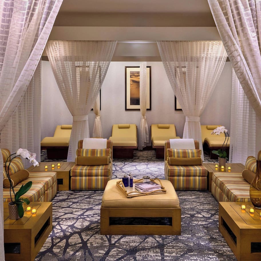 A spa room with multiple massage chairs, a central ottoman with books and a vase, and a patterned carpet.
