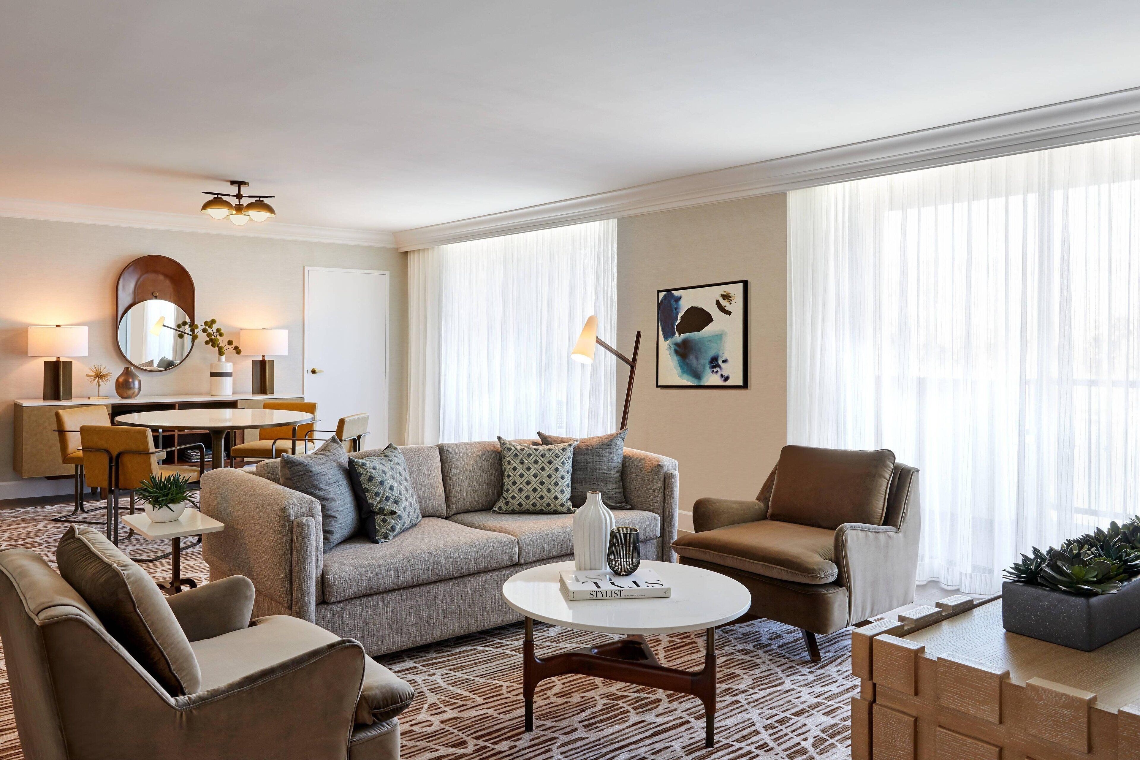 A modern living room with a sofa, armchairs, a coffee table, and a dining area with a table and chairs.