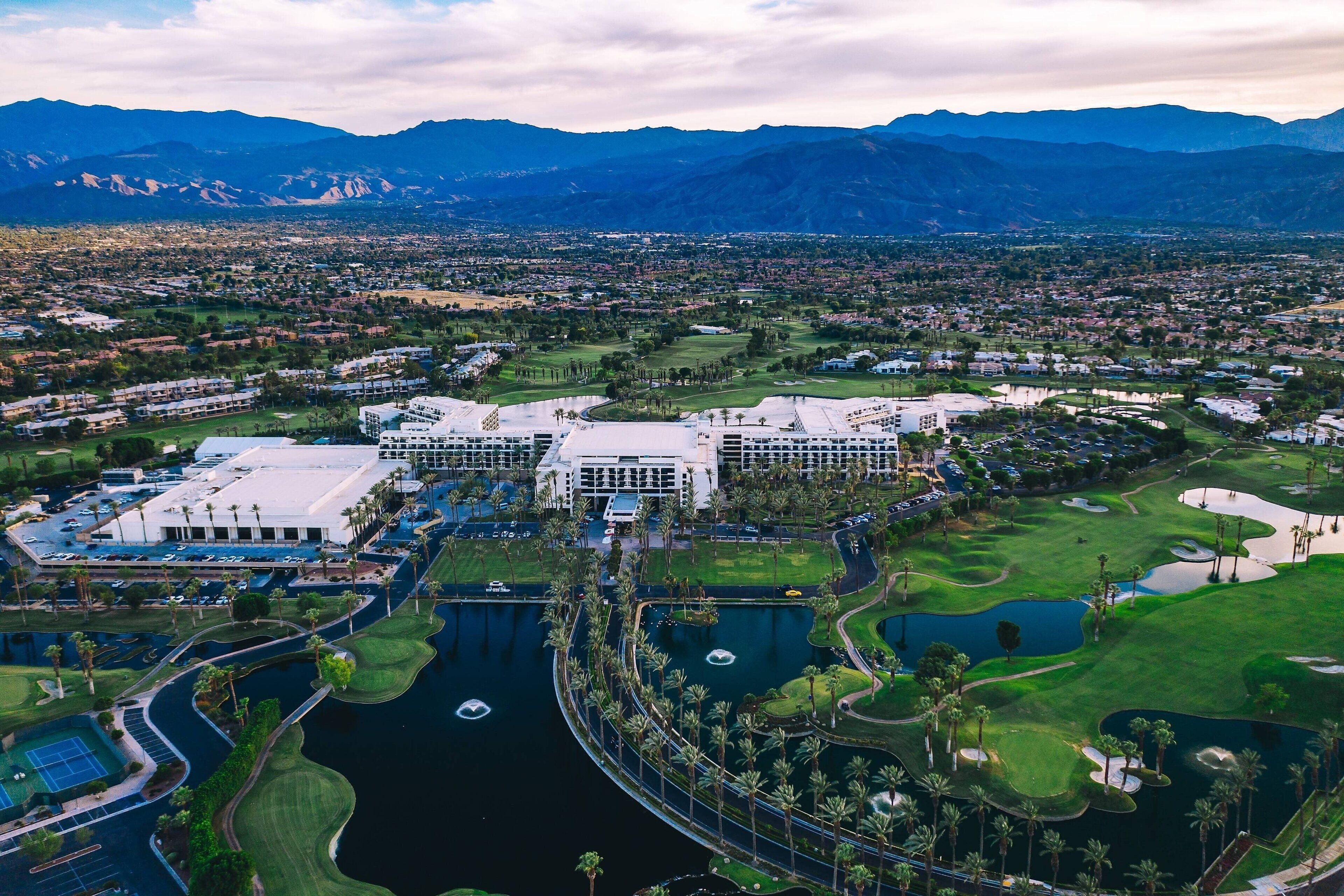 An aerial view of a golf course with a large building complex, water features, and surrounding residential areas.