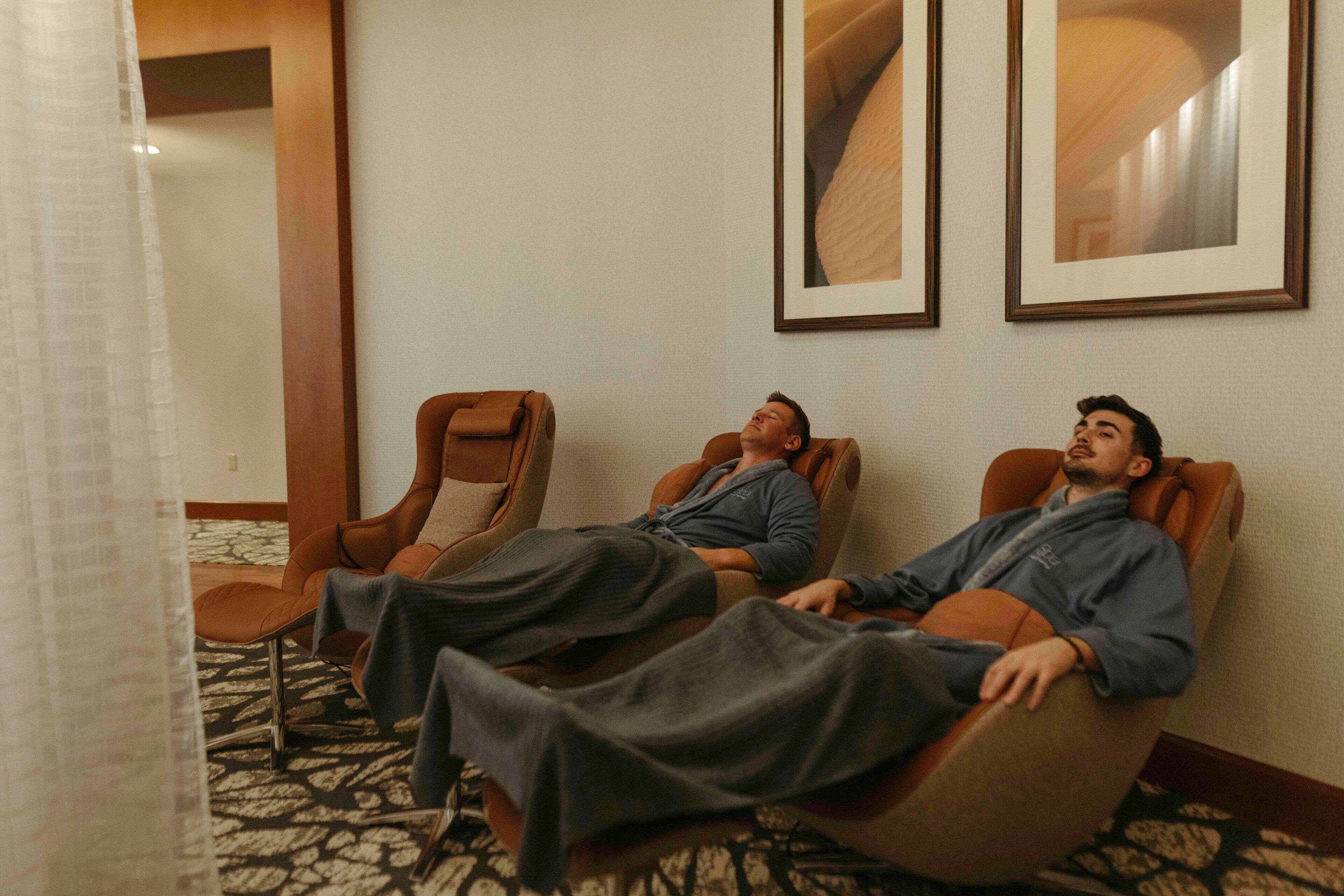 Two massage chairs in a room with a patterned carpet and framed artwork on the wall.