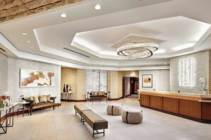 A spacious lobby with a reception desk, seating areas, and a modern chandelier.