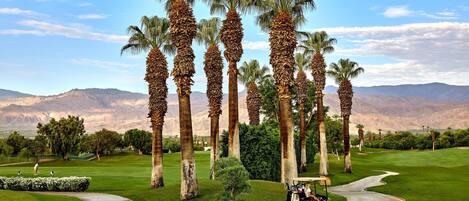 A golf course with palm trees, a golf cart, and a mountainous backdrop.