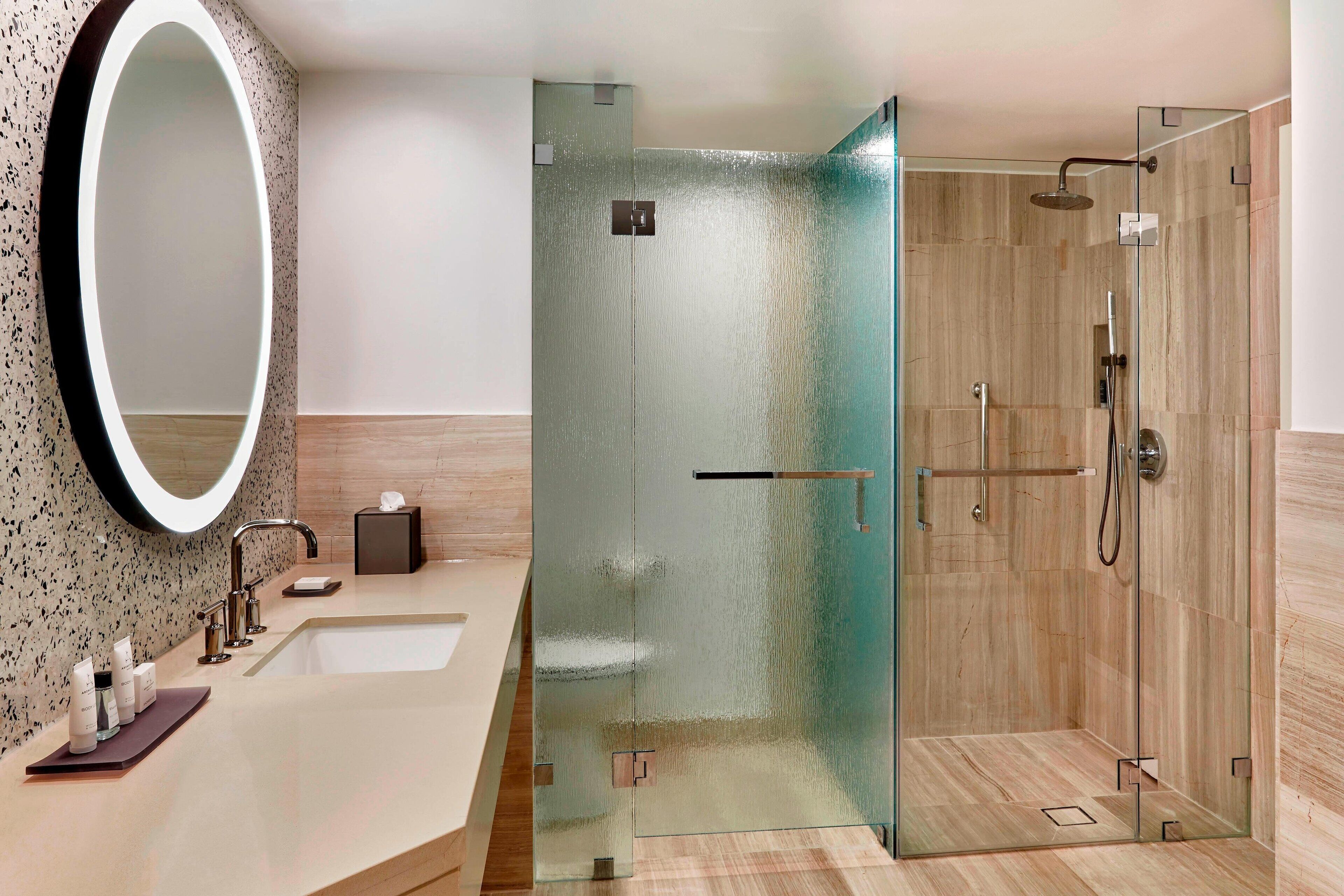 A modern bathroom with a glass-enclosed shower, a large mirror, and a countertop with toiletries.