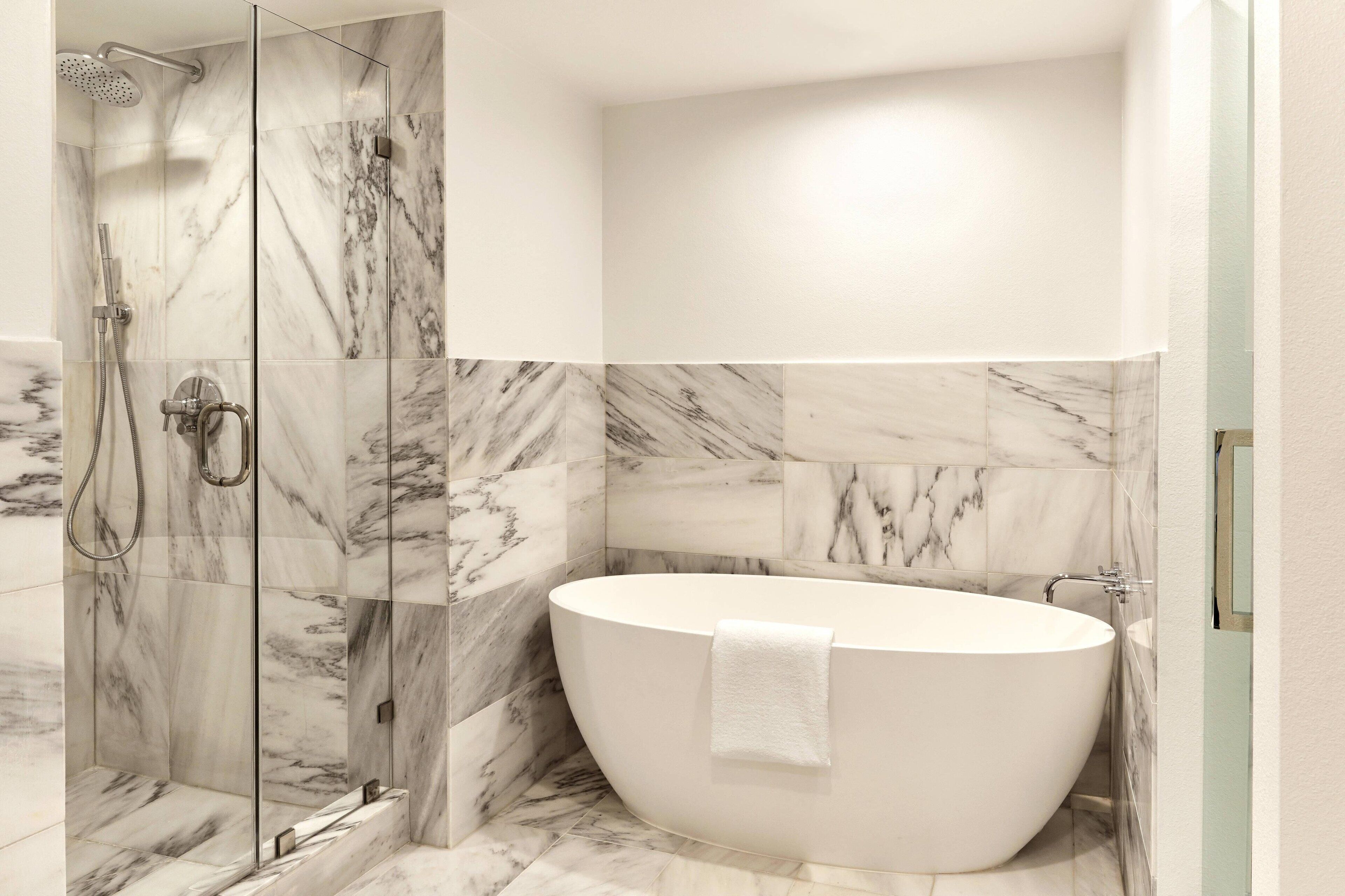 A modern bathroom with a freestanding bathtub, a glass-enclosed shower, and marble flooring.