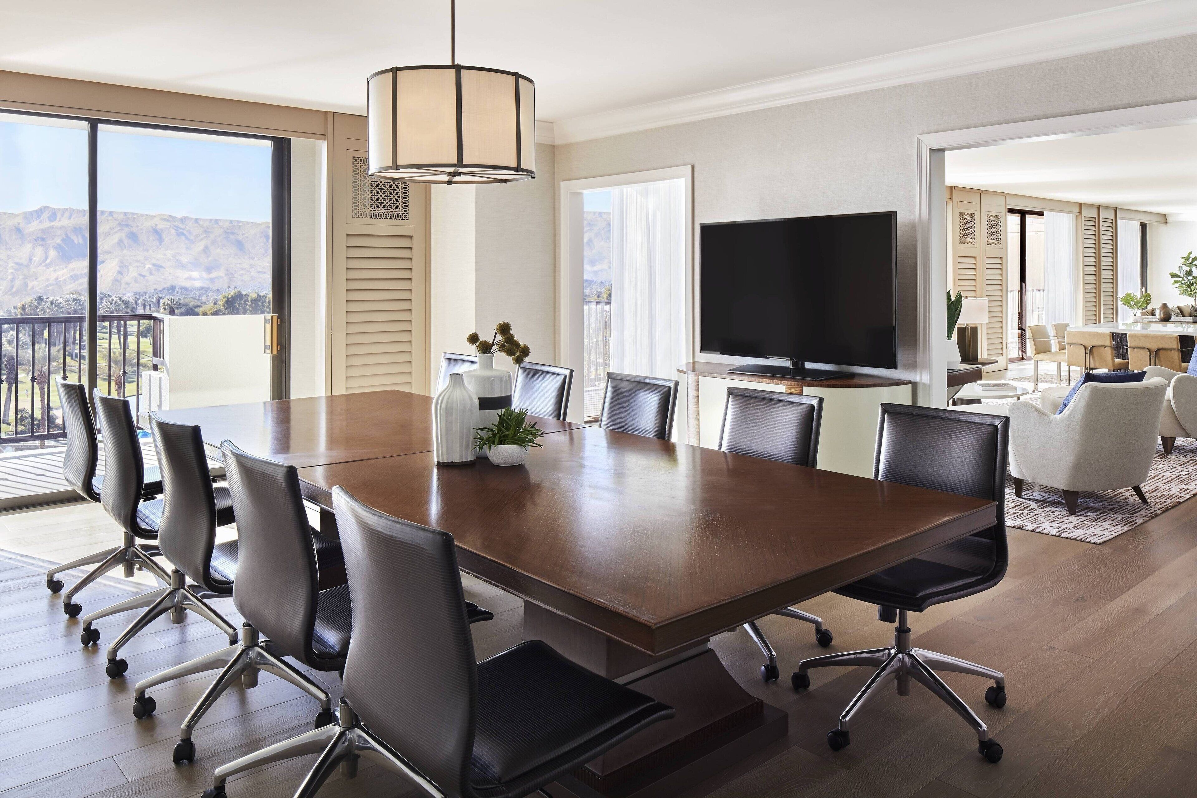 A conference room with a large table, chairs, a TV, and a view of the mountains.