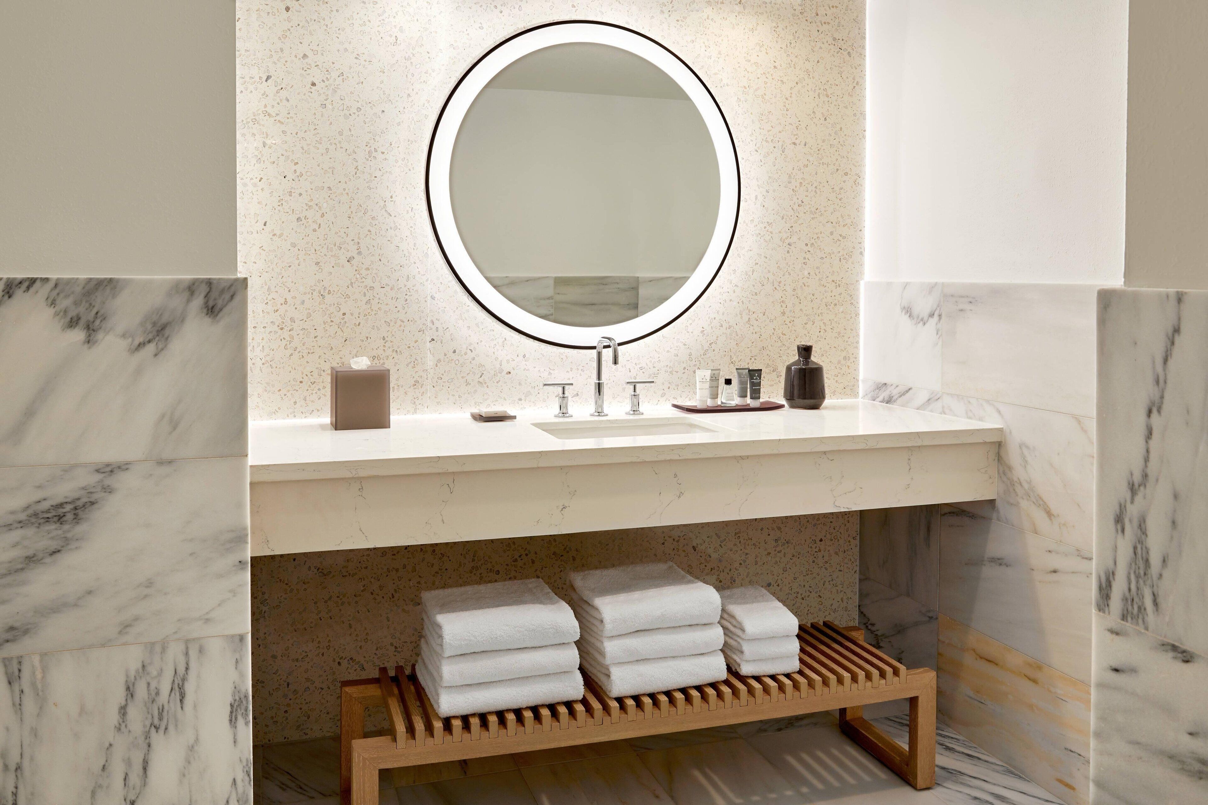 A bathroom with a marble sink, a round mirror, and a wooden towel rack.