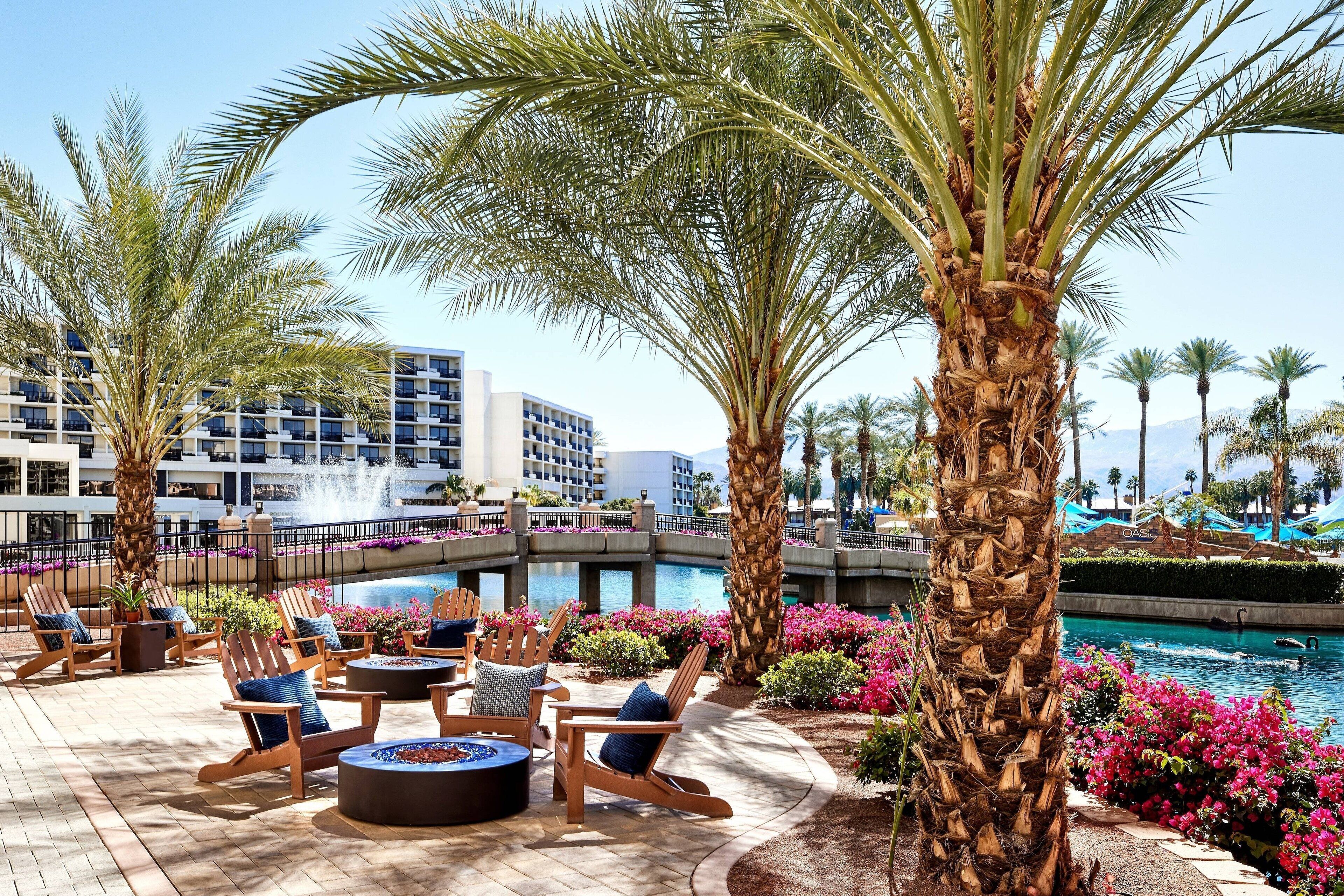A poolside area with lounge chairs, a fire pit, and palm trees.