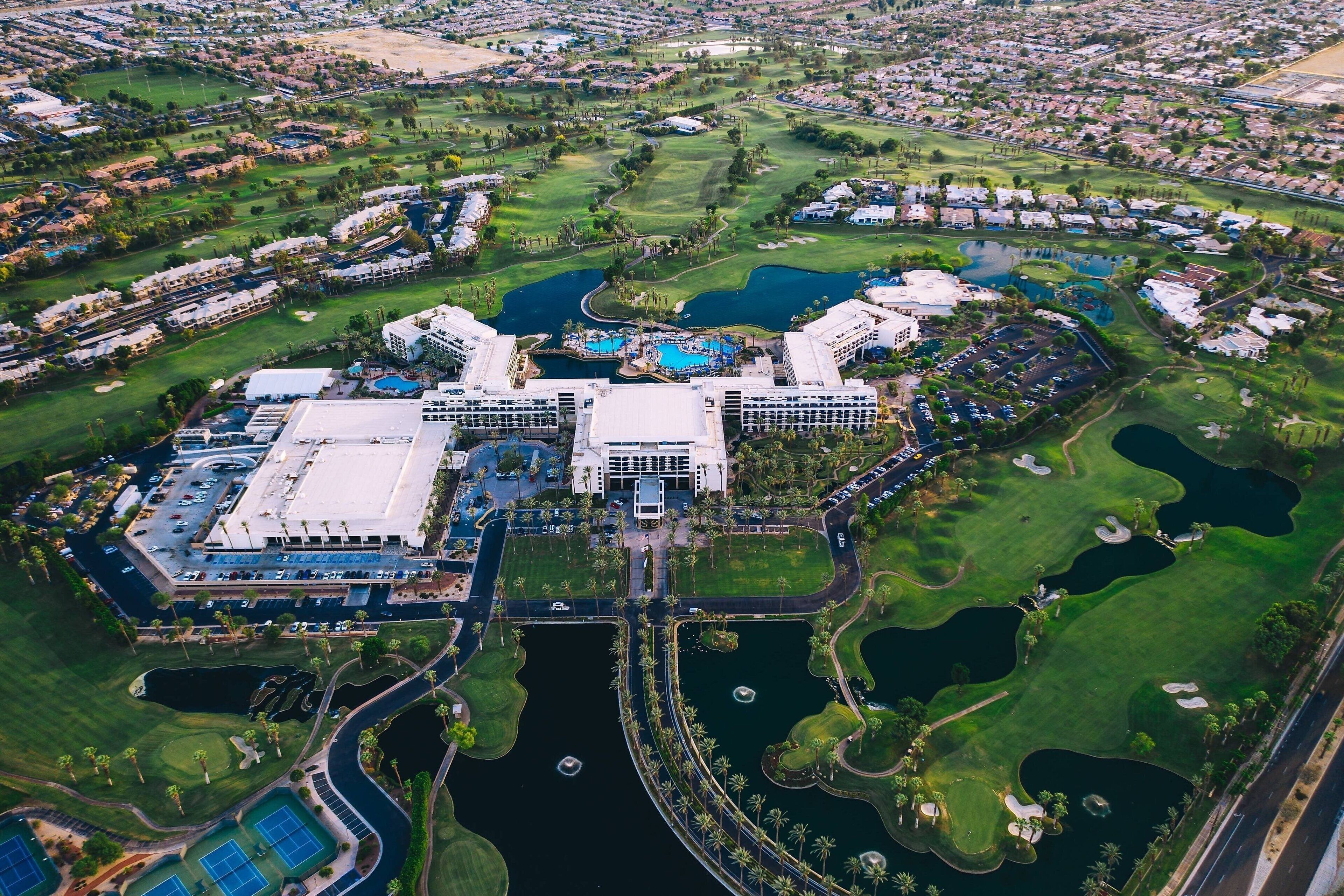 Vista aèria d'un complex de golf amb diversos edificis, una zona de piscina central i espais verds circumdants.