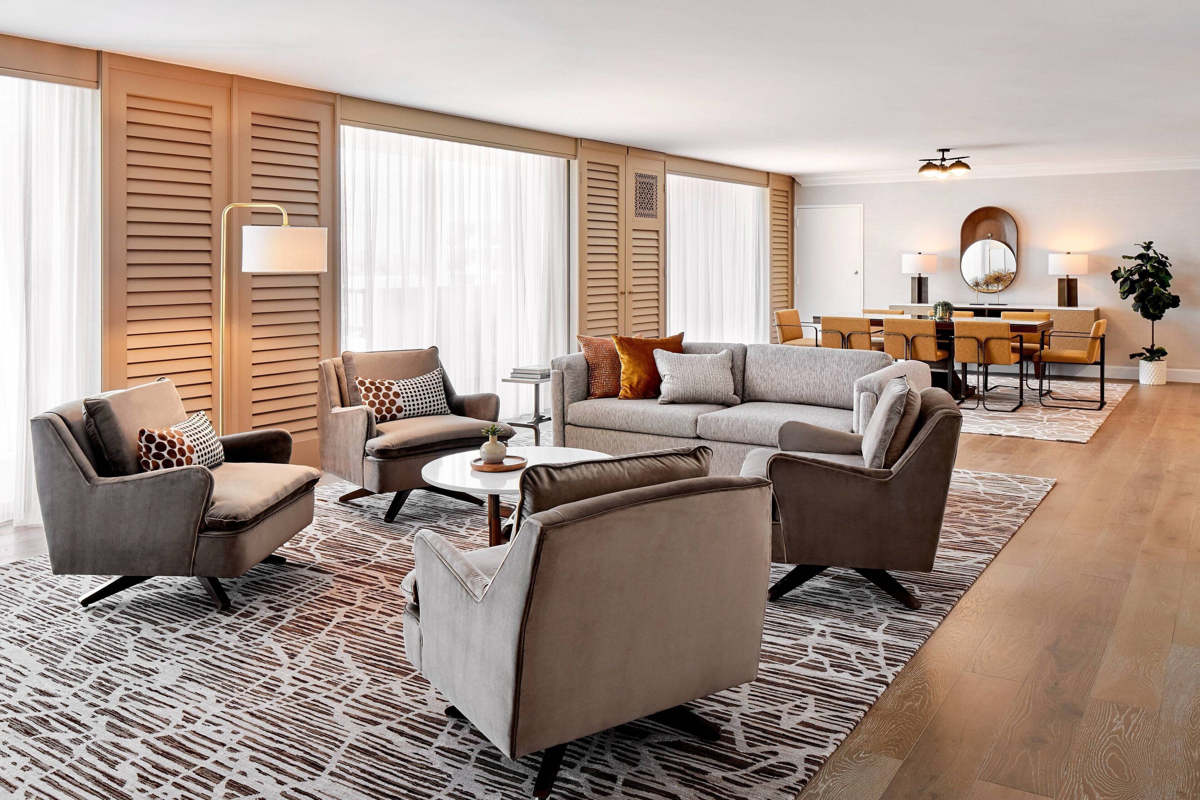 A modern living room with a sofa, armchairs, a coffee table, and a dining area with chairs and a table.