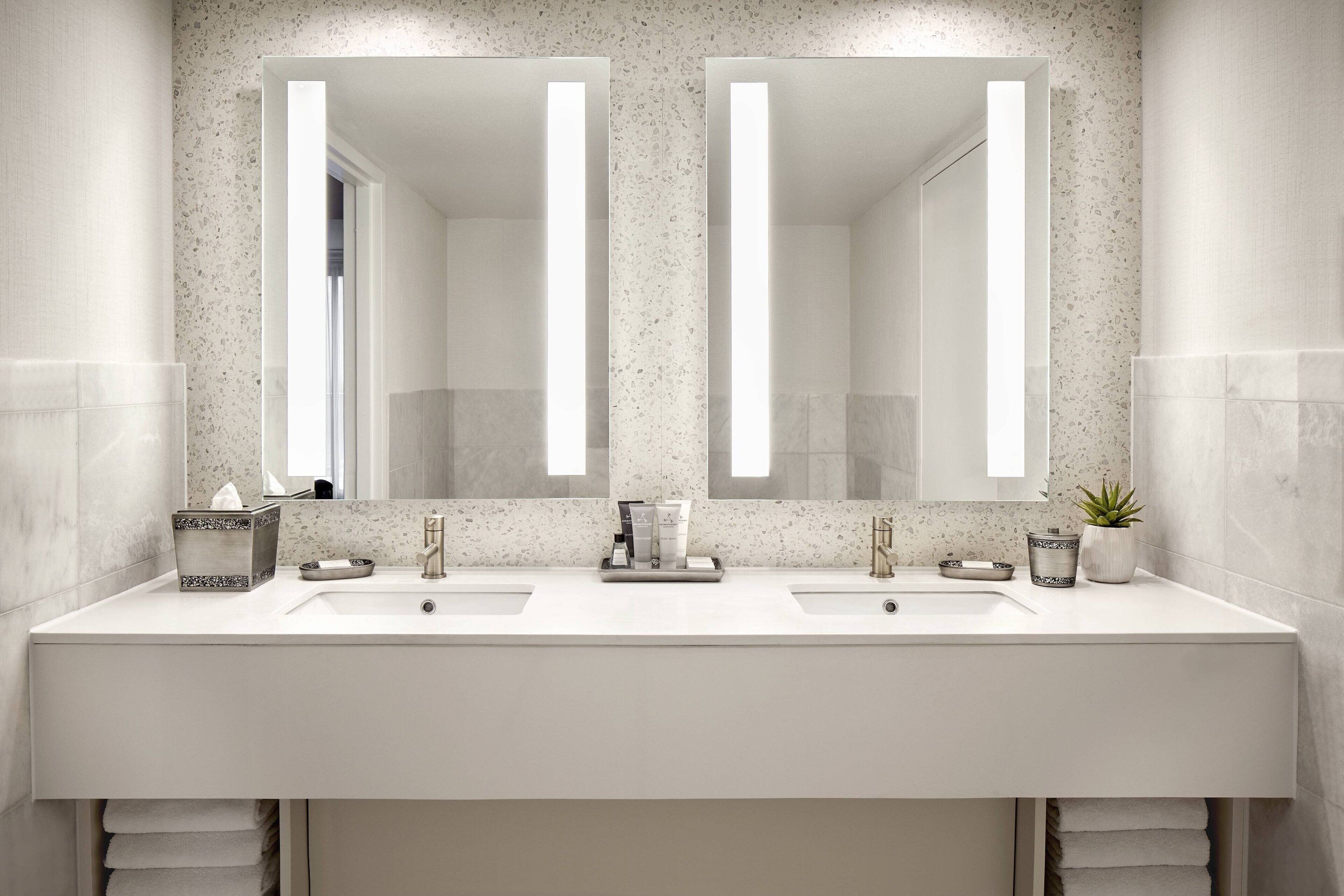 A modern bathroom with two sinks, a large mirror, and a towel rack.