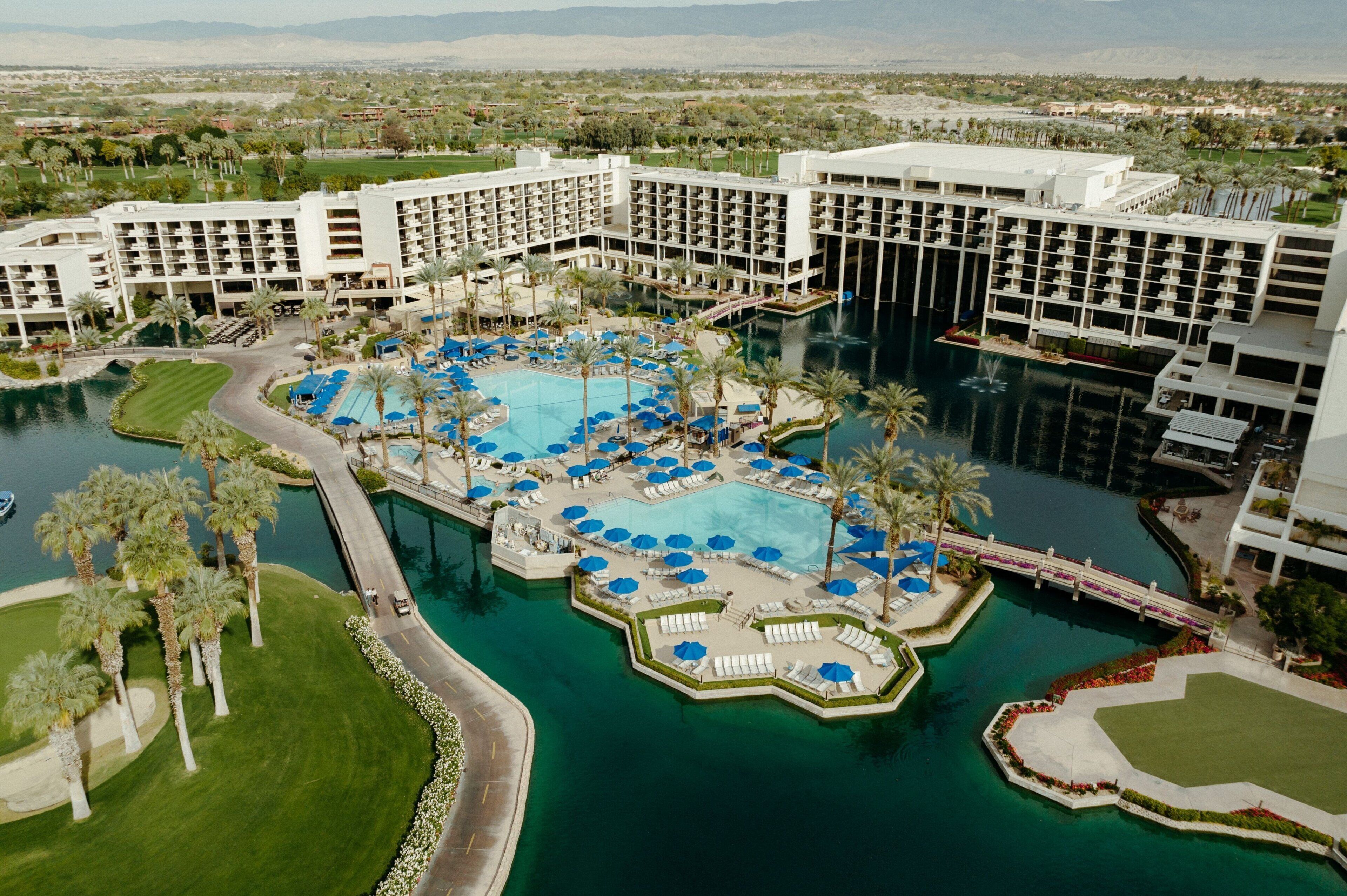 A large hotel with multiple swimming pools, palm trees, and a golf course.