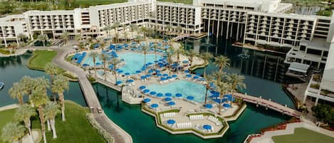 A large hotel with multiple swimming pools, palm trees, and a golf course.