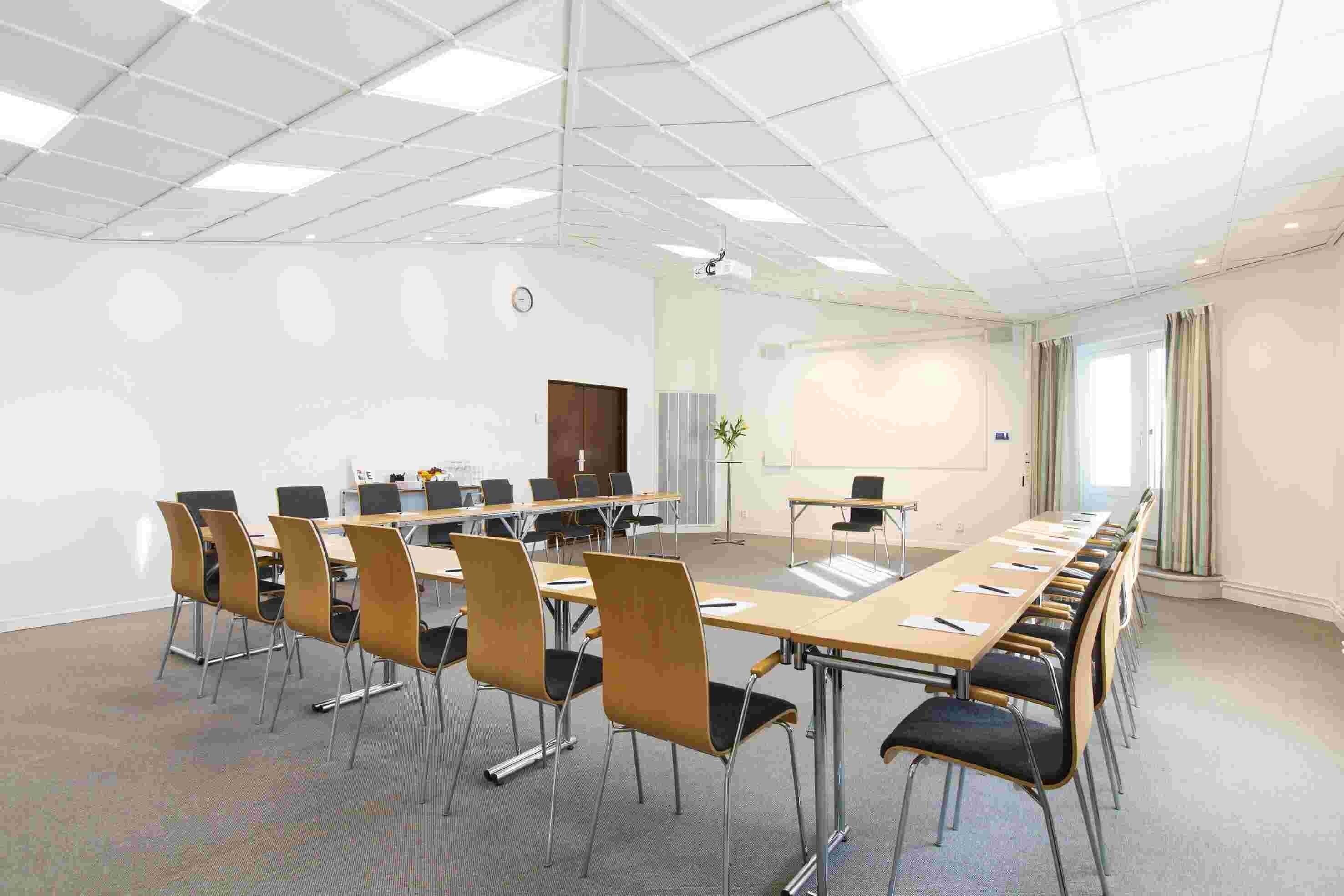 Une salle de conférence équipée d’une longue table, de chaises, d’un écran de projection et d’un tableau blanc.