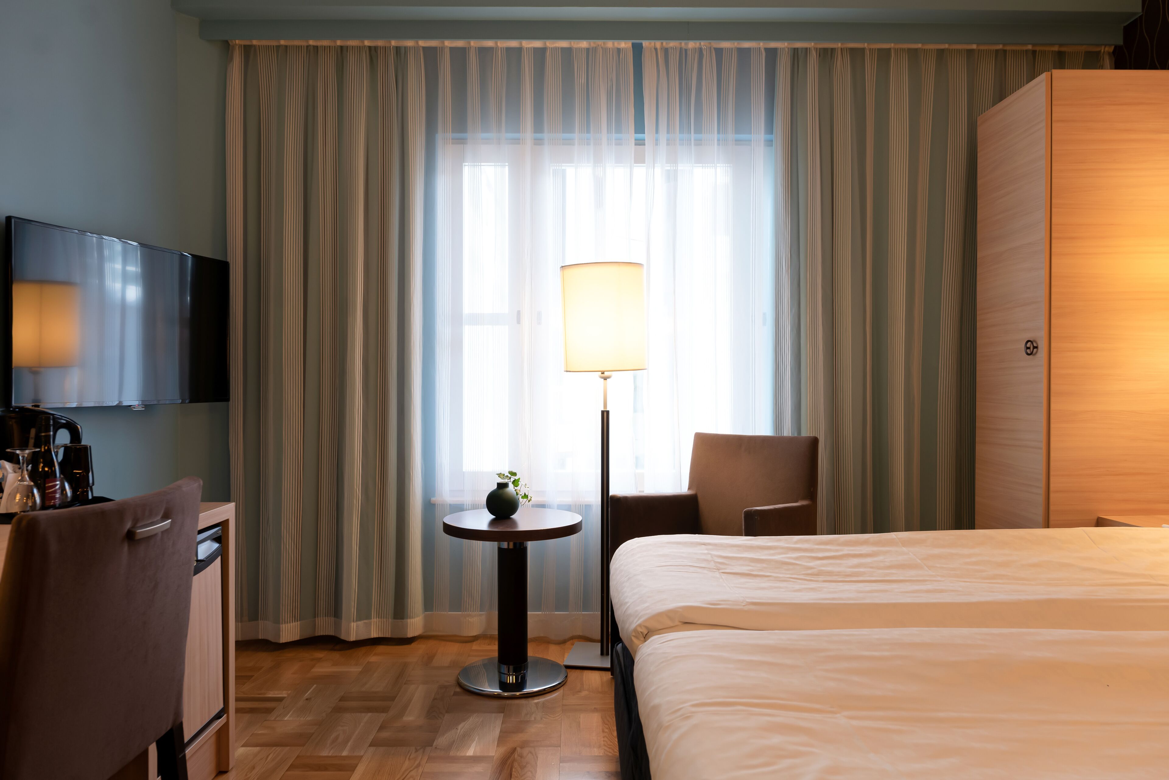 Ein Hotelzimmer mit Bett, Schreibtisch mit Lampe, Fernseher und großem Kleiderschrank.