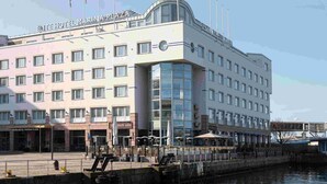 Een hotel met meerdere verdiepingen, met een moderne gevel, een opvallend gebogen glazen gedeelte en diverse vlaggen.