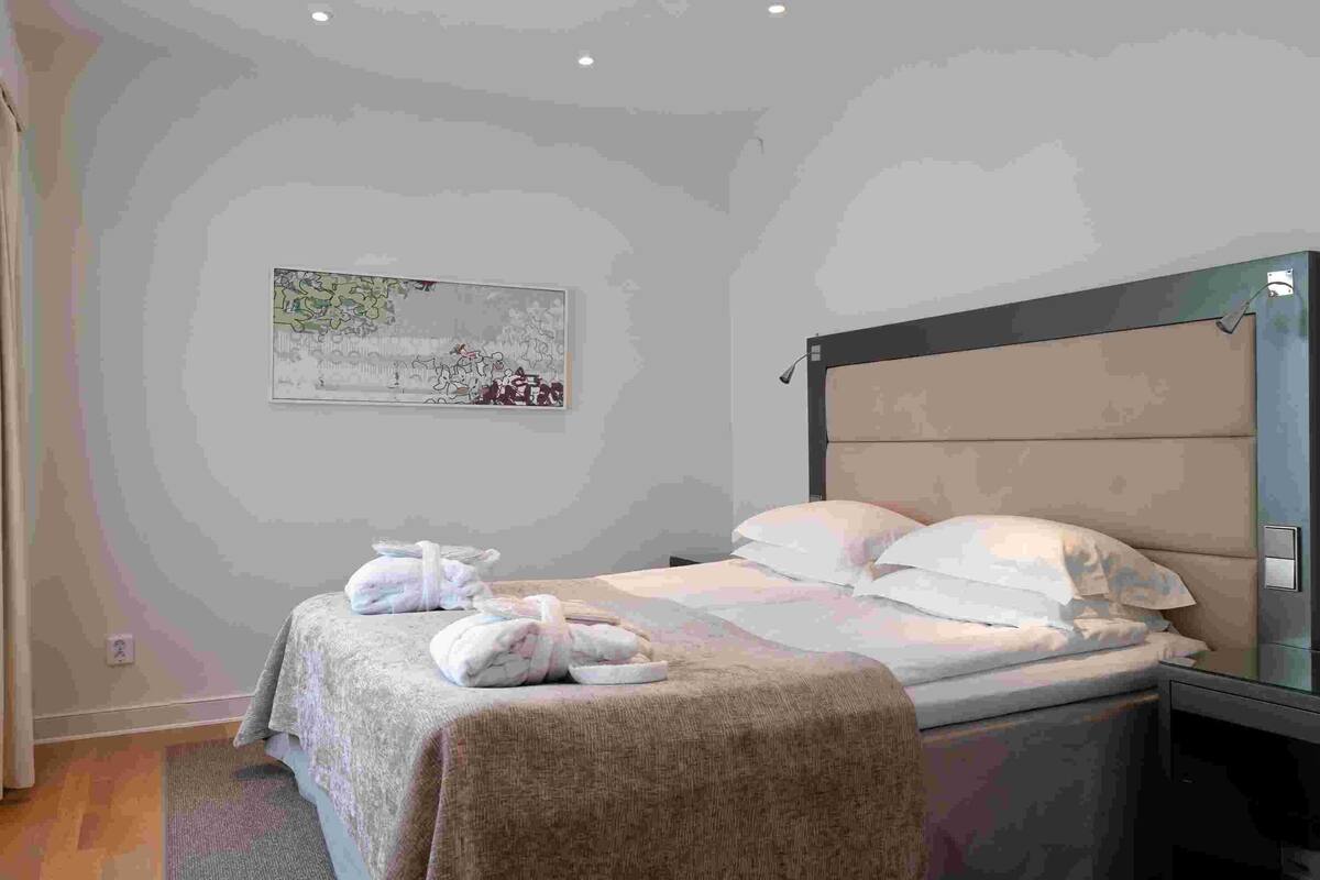 Een hotelkamer met een bed, een hoofdbord, een nachtkastje, een aan de muur hangend schilderij en een raam.