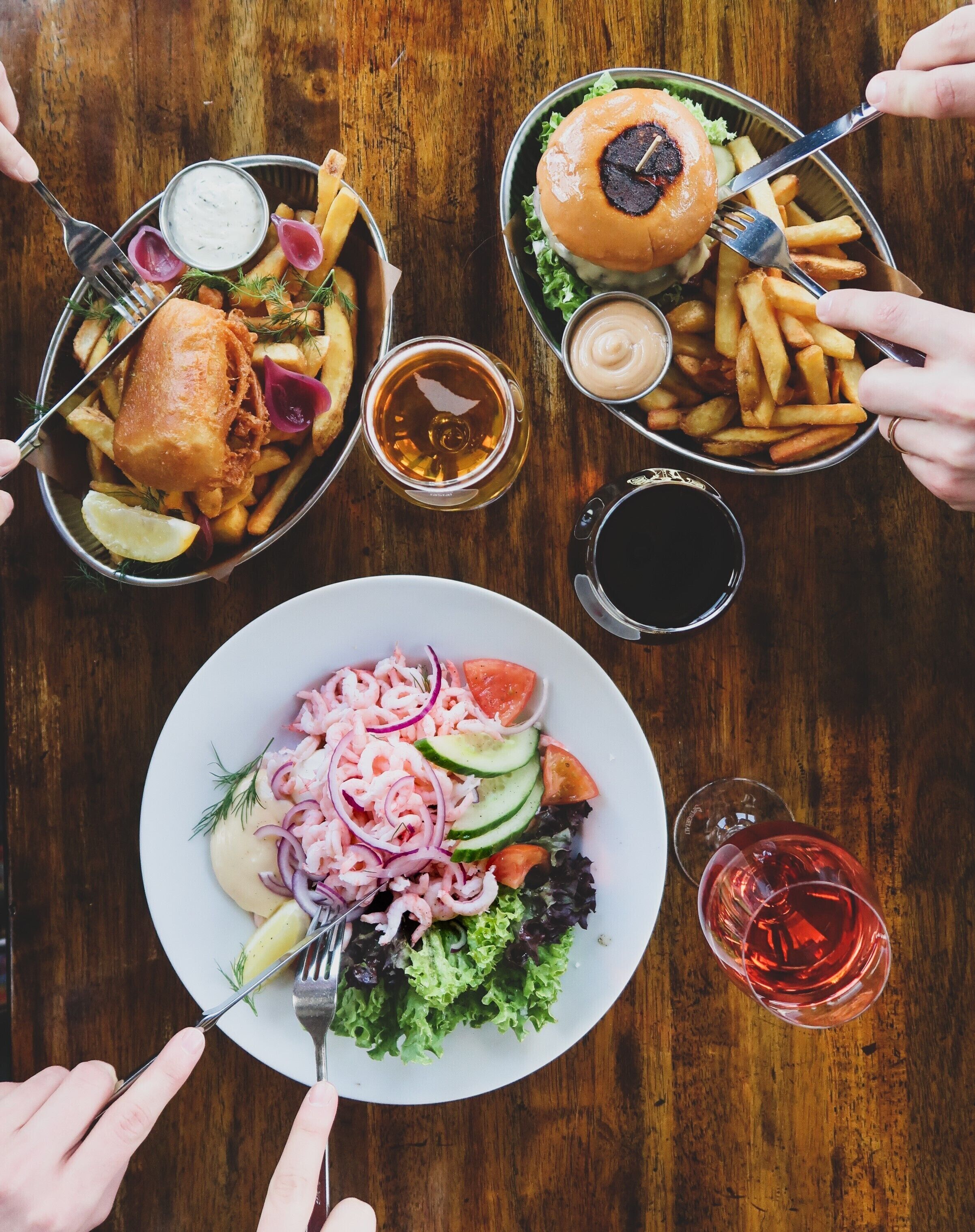 A table with various dishes including fish and chips, burgers, and a salad, along with drinks and utensils.