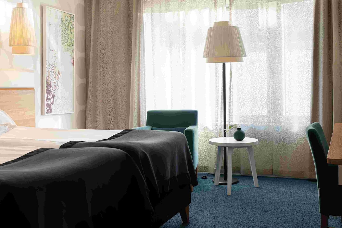 Een hotelkamer met een bed, twee stoelen, een klein tafeltje met een vaas en een lamp.
