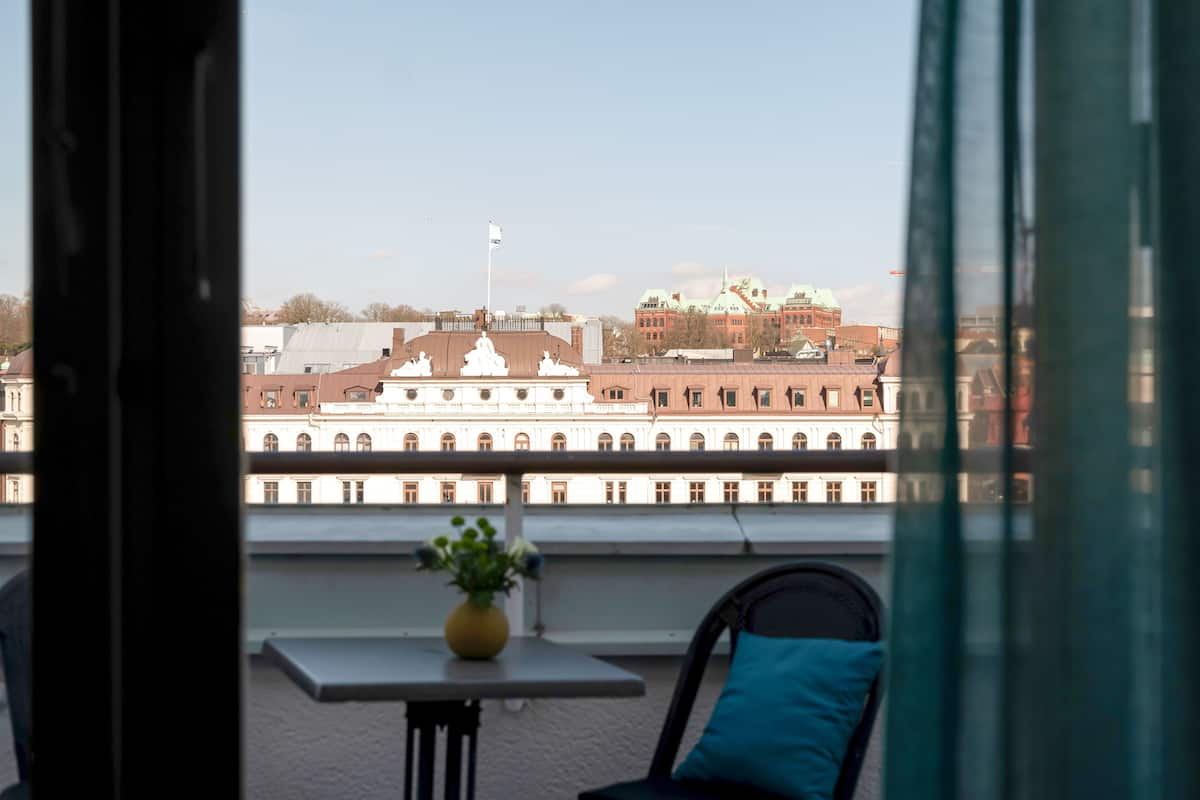 Een balkon met een tafel en stoel, met uitzicht op een historisch gebouw met meerdere ramen en een vlag.