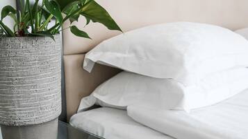 A modern bedroom with a bed, white pillows, and a potted plant on a bedside table.