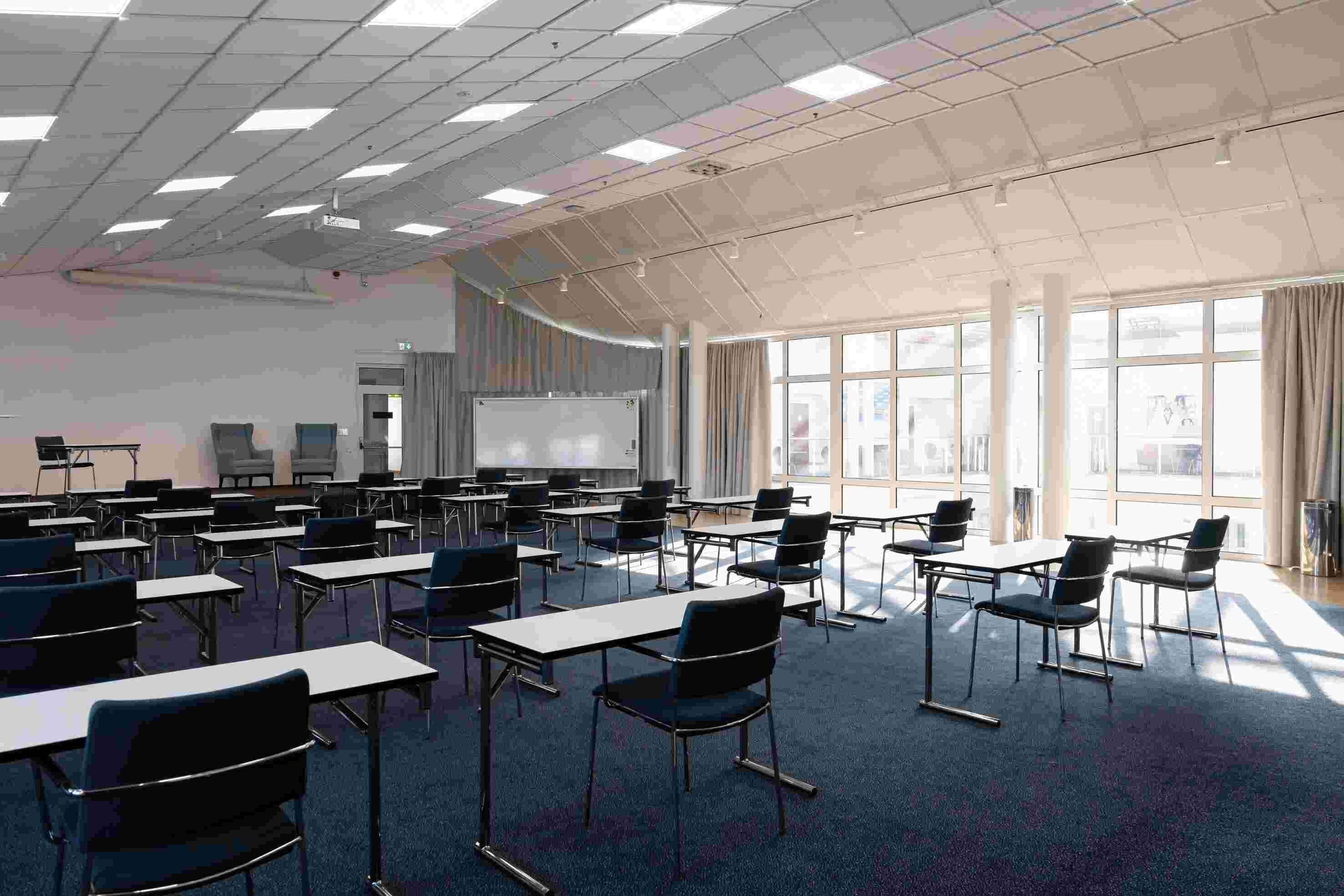 A classroom with desks and chairs arranged in rows, a whiteboard, and a projector screen.