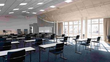 A classroom with desks and chairs arranged in rows, a whiteboard, and a projector screen.