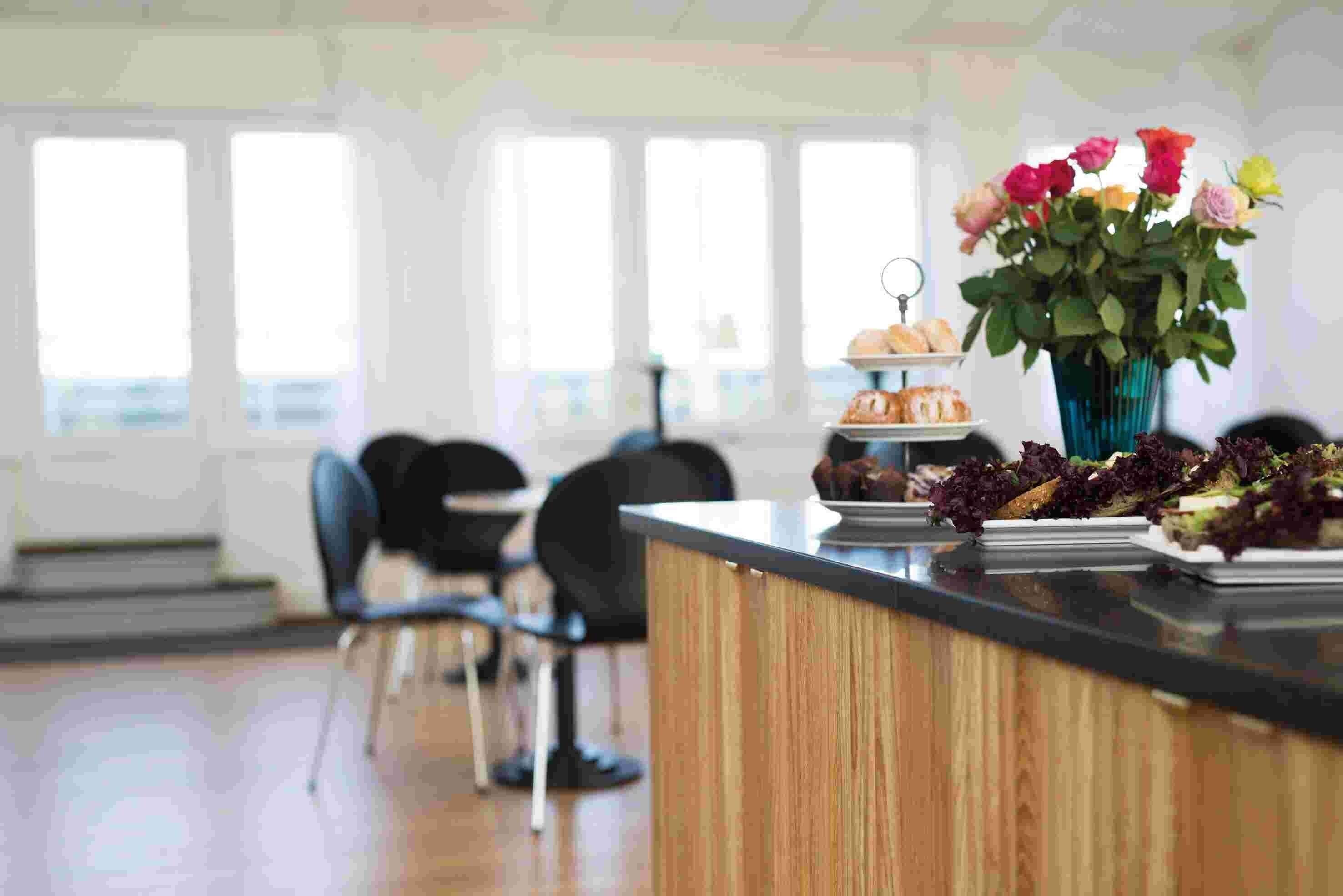 Uma área de recepção com balcão de madeira, um vaso de flores e um buffet com diversos alimentos.