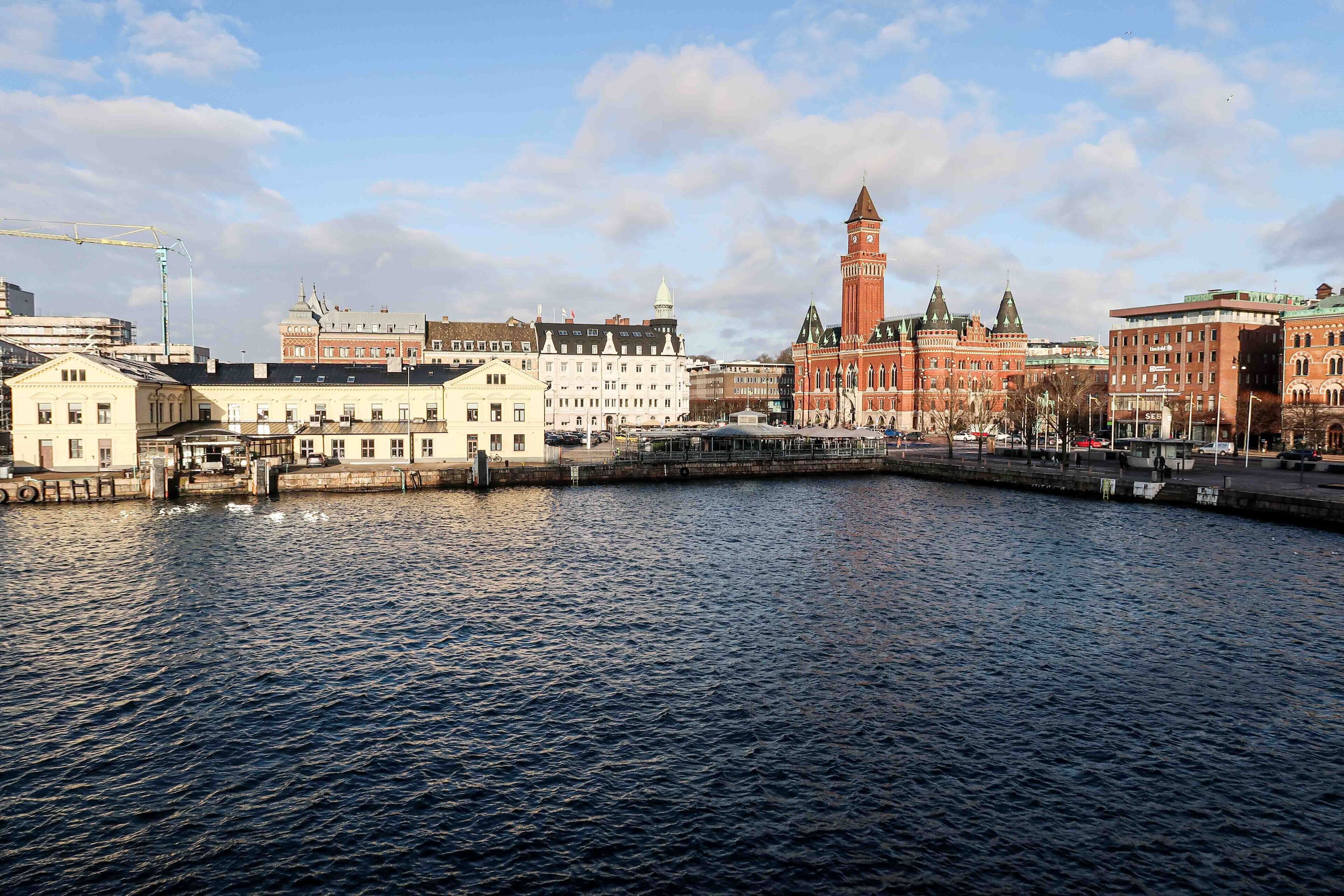 Un paysage urbain au bord de l’eau, avec des bâtiments historiques, une tour imposante et une rivière paisible.