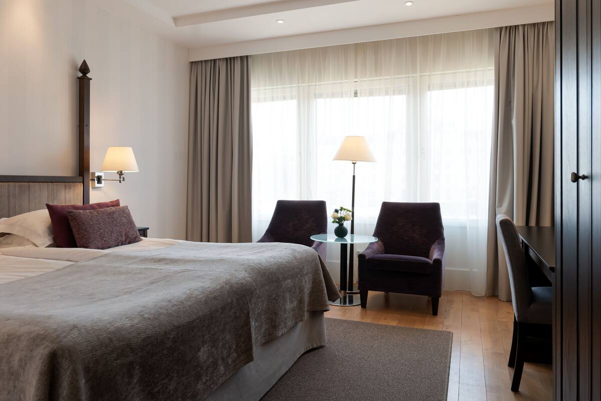 Een moderne hotelkamer met een groot bed, twee fauteuils, een tafeltje en een bureau.