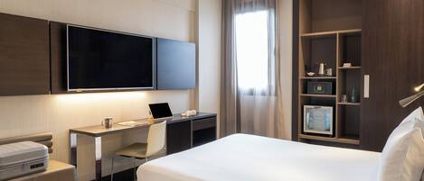 Une chambre d’hôtel équipée d’un lit, d’un bureau, d’une chaise, d’une télévision et d’étagères intégrées où sont rangés divers objets.