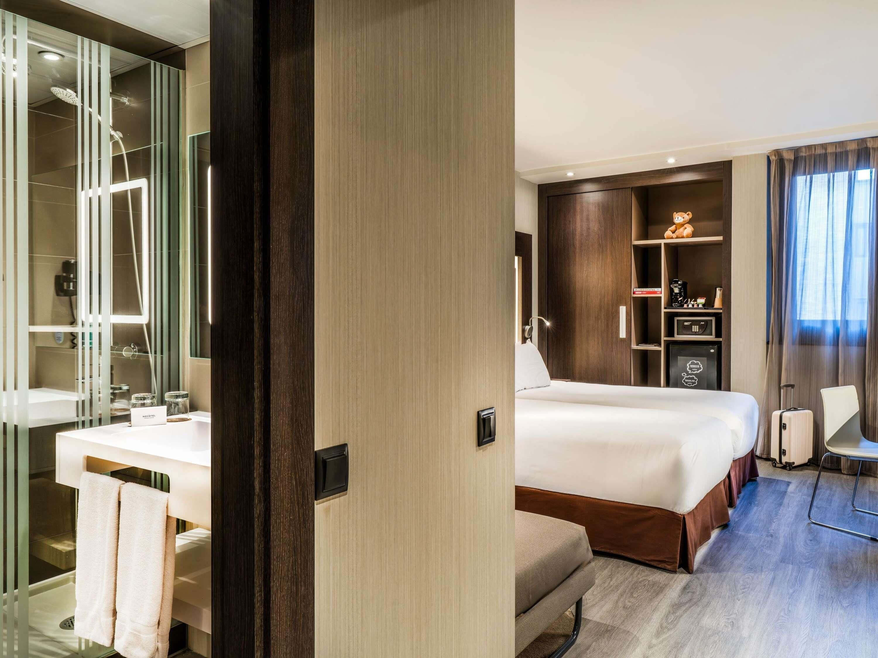 A hotel room with a bed, a desk, a chair, a wardrobe, and a bathroom with a shower.