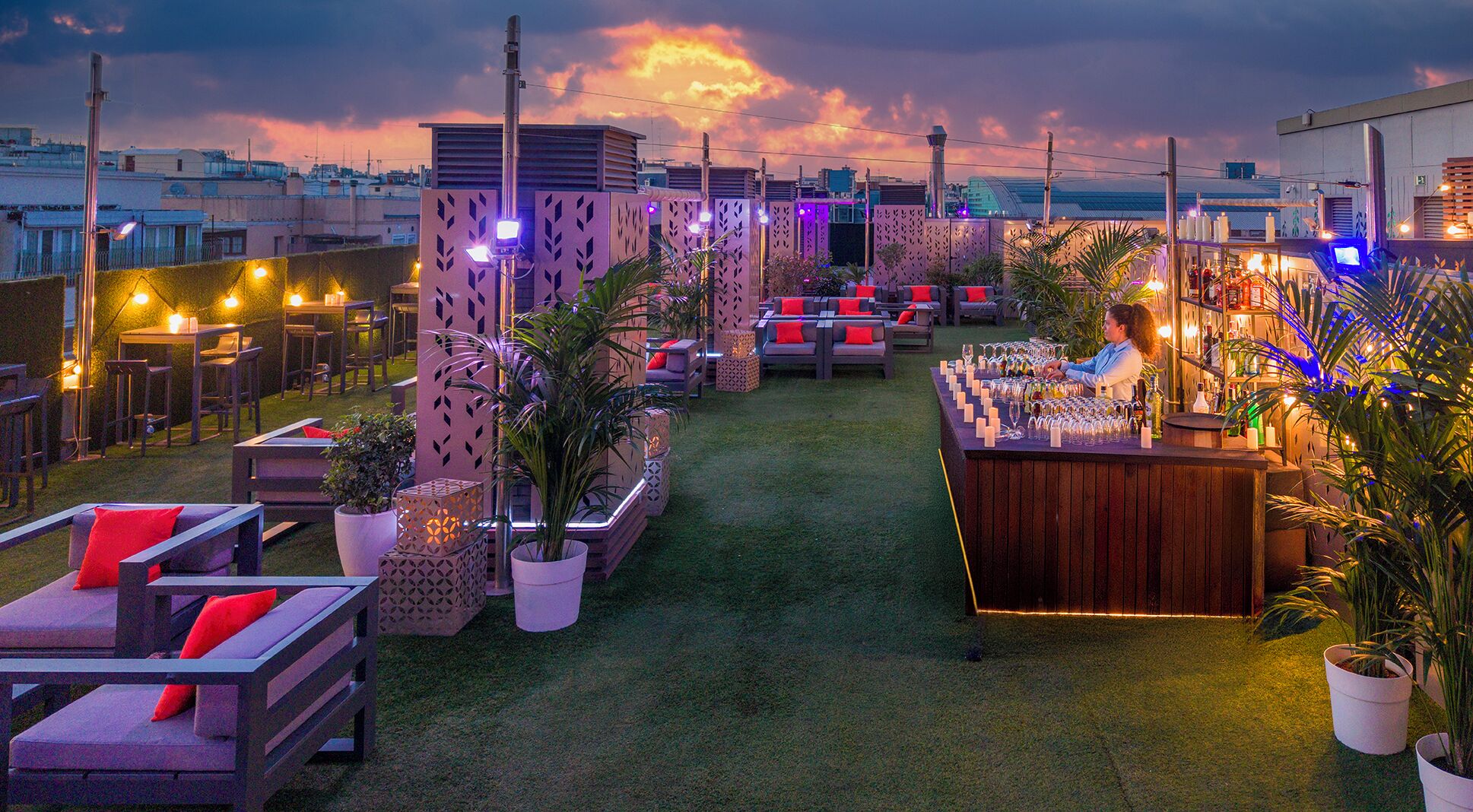 An outdoor bar area with seating, a bartender, and a cityscape view.