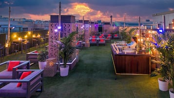An outdoor bar area with seating, a bartender, and a cityscape view.