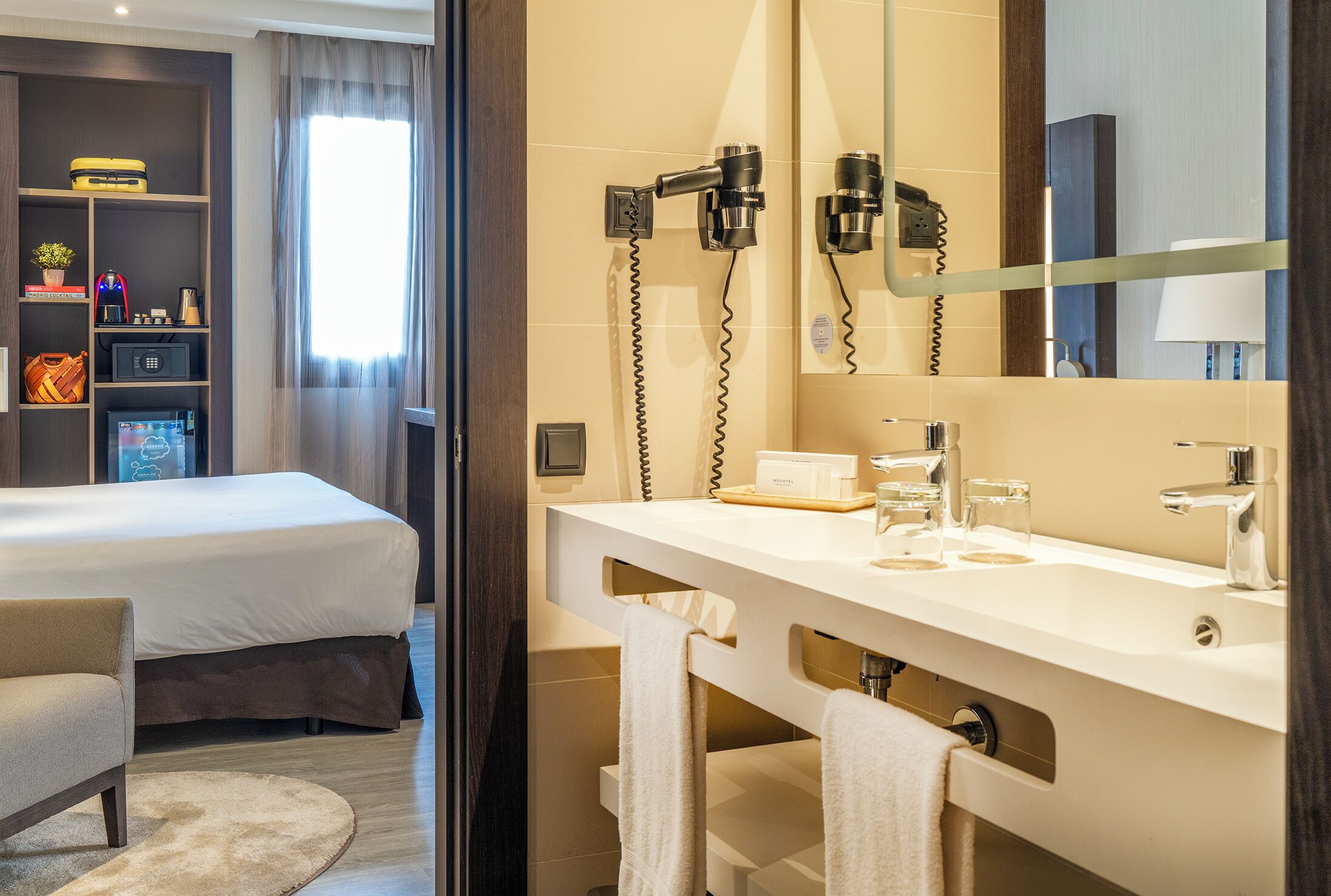 A hotel room with a bed, a sofa, a bathroom with a sink, mirror, and hairdryer.