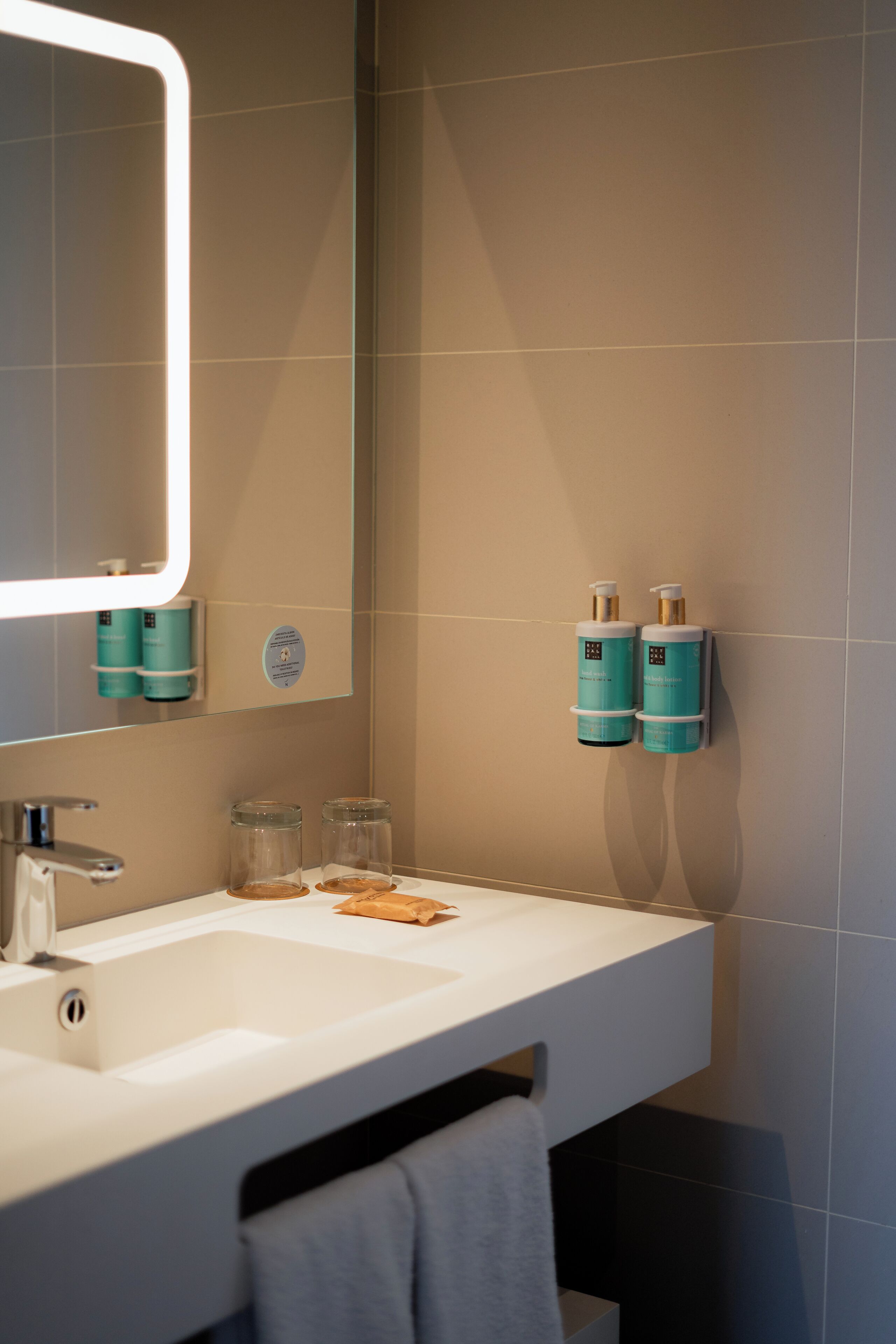 Un baño moderno con un lavamanos blanco, un espejo con luz y dos dispensadores verde azulado en la pared.