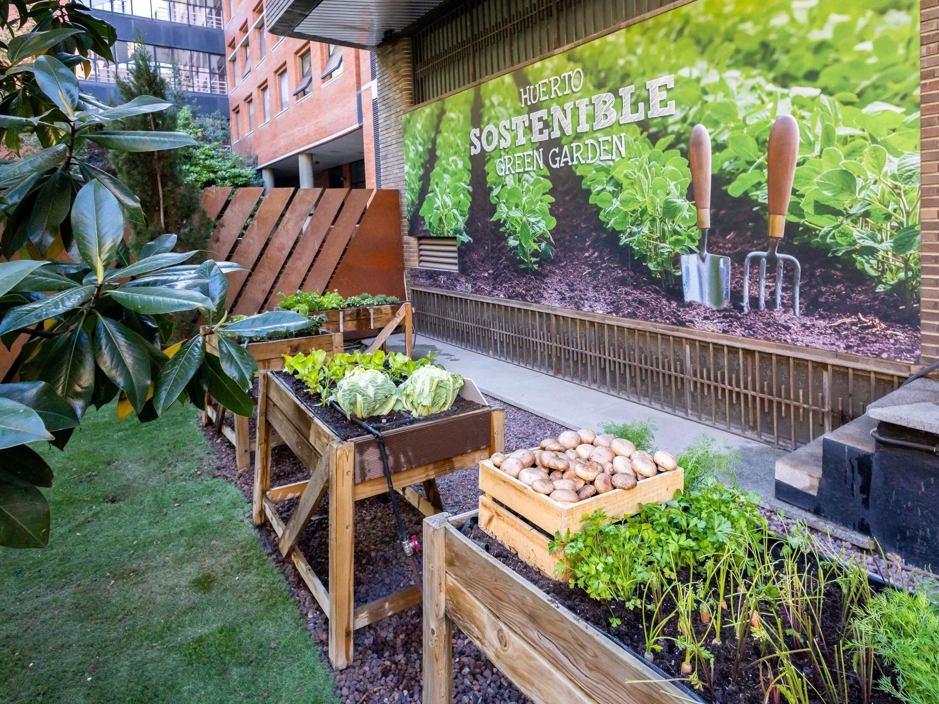 Un giardino pensile con aiuole rialzate, una panchina di legno e un murale raffigurante attrezzi da giardinaggio.