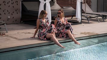 Zwei Personen entspannen an einem Pool mit Sonnensegel und Liegestühlen.