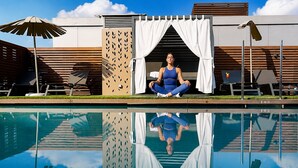 Un espace aménagé au bord de la piscine, avec une personne assise près de la piscine, un rideau blanc et le chiffre « 105 » inscrit sur le bord de la piscine.