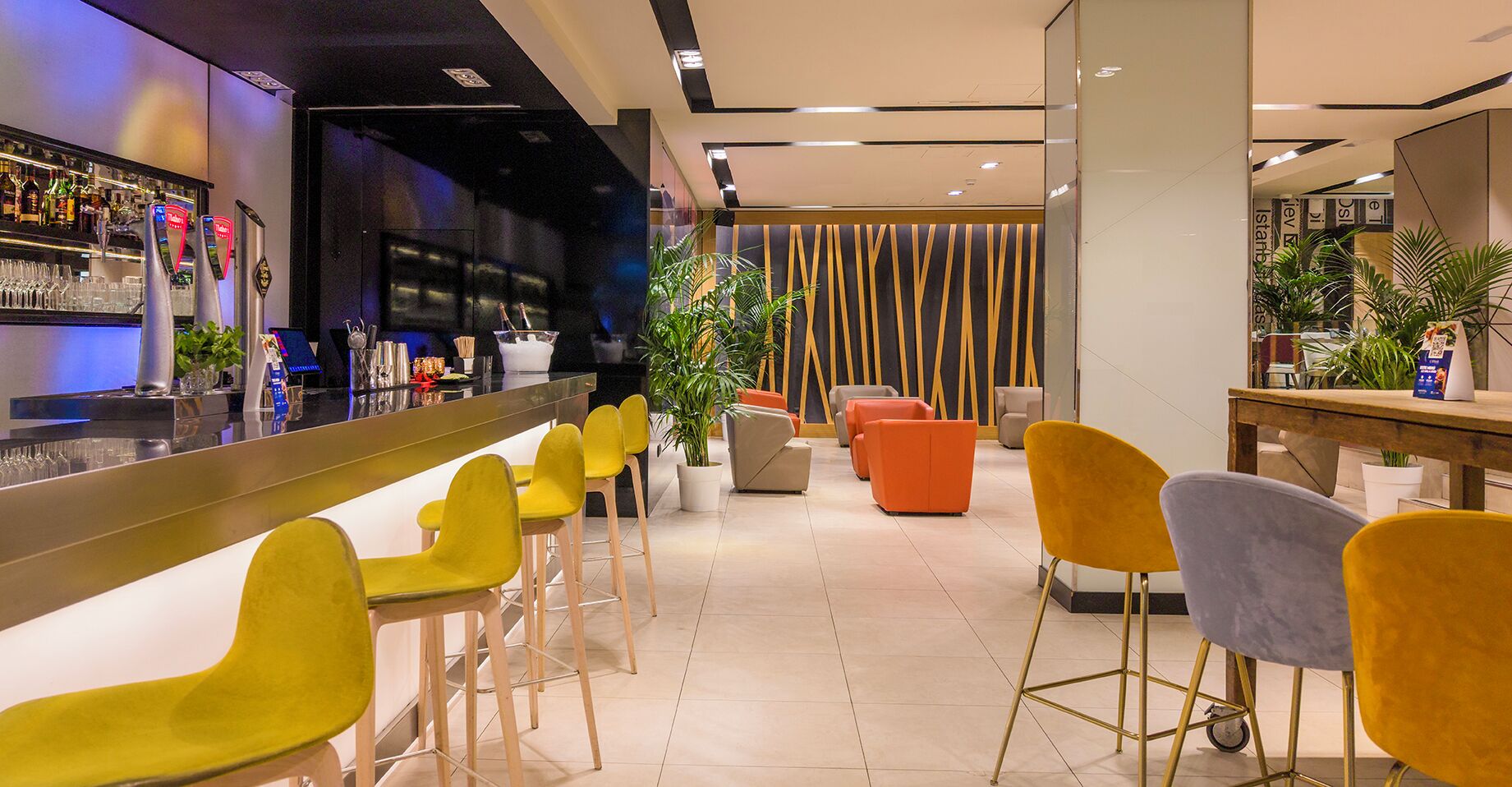 Zona de bar con taburetes, una barra y un área de asientos con sillas.