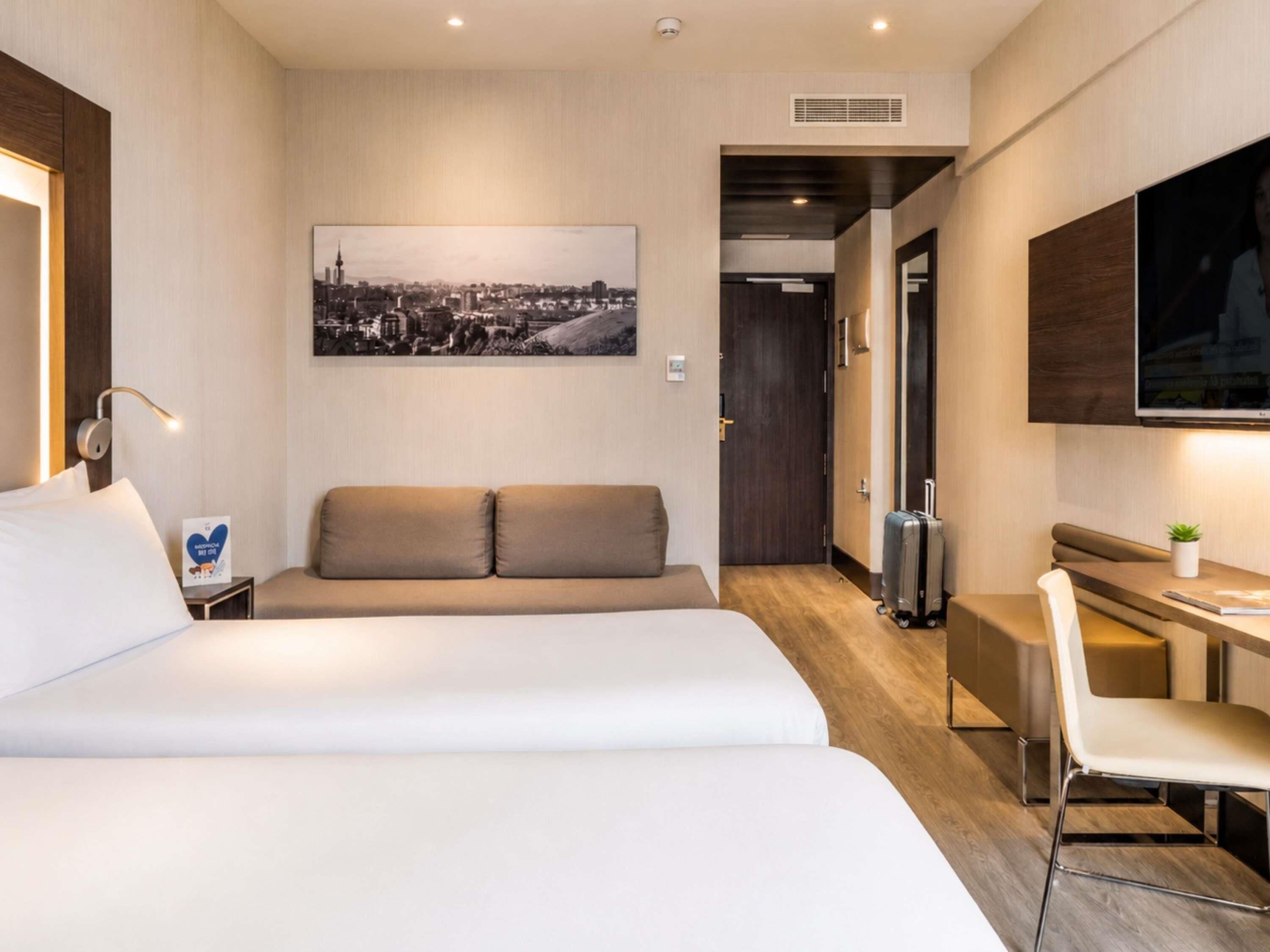 A hotel room with a bed, a sofa, a desk, and a television.