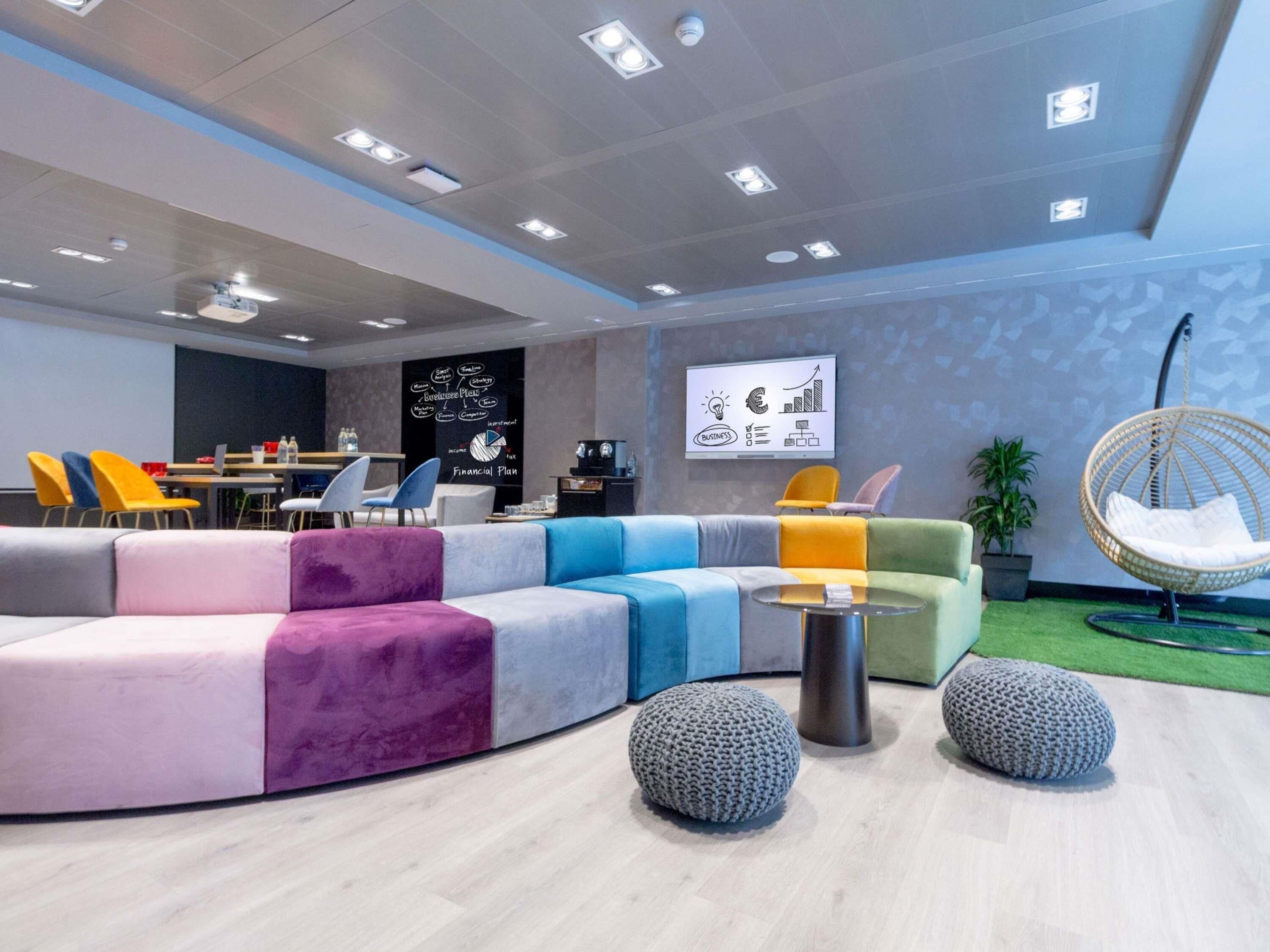 A modern lounge area with a curved sofa, round ottomans, a hanging chair, and a presentation screen.