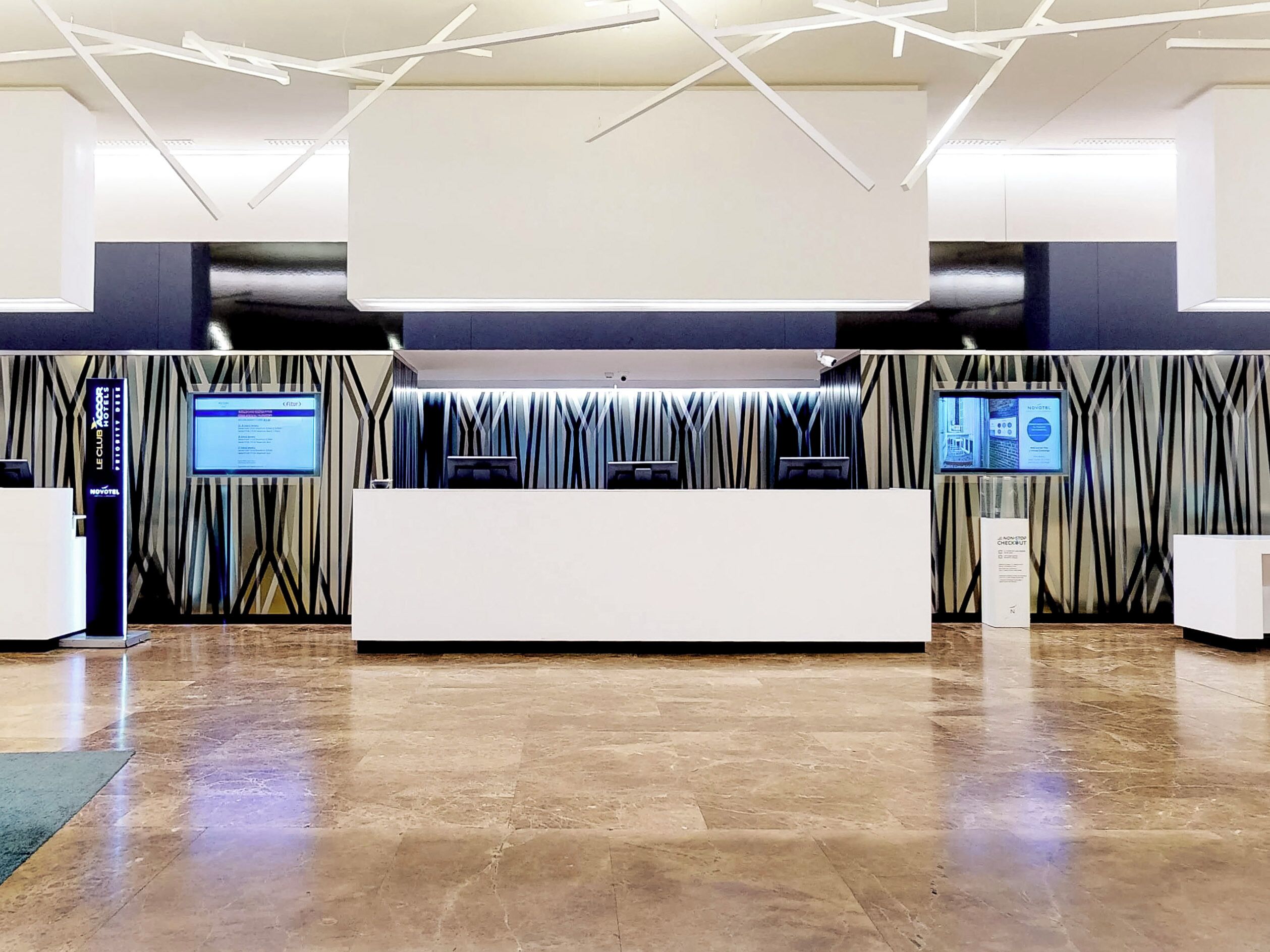 Zona de recepción moderna de hotel con un mostrador central, pantallas digitales y una pared con diseño.