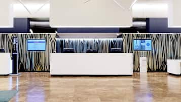 Zona de recepción moderna de hotel con un mostrador central, pantallas digitales y una pared con diseño.